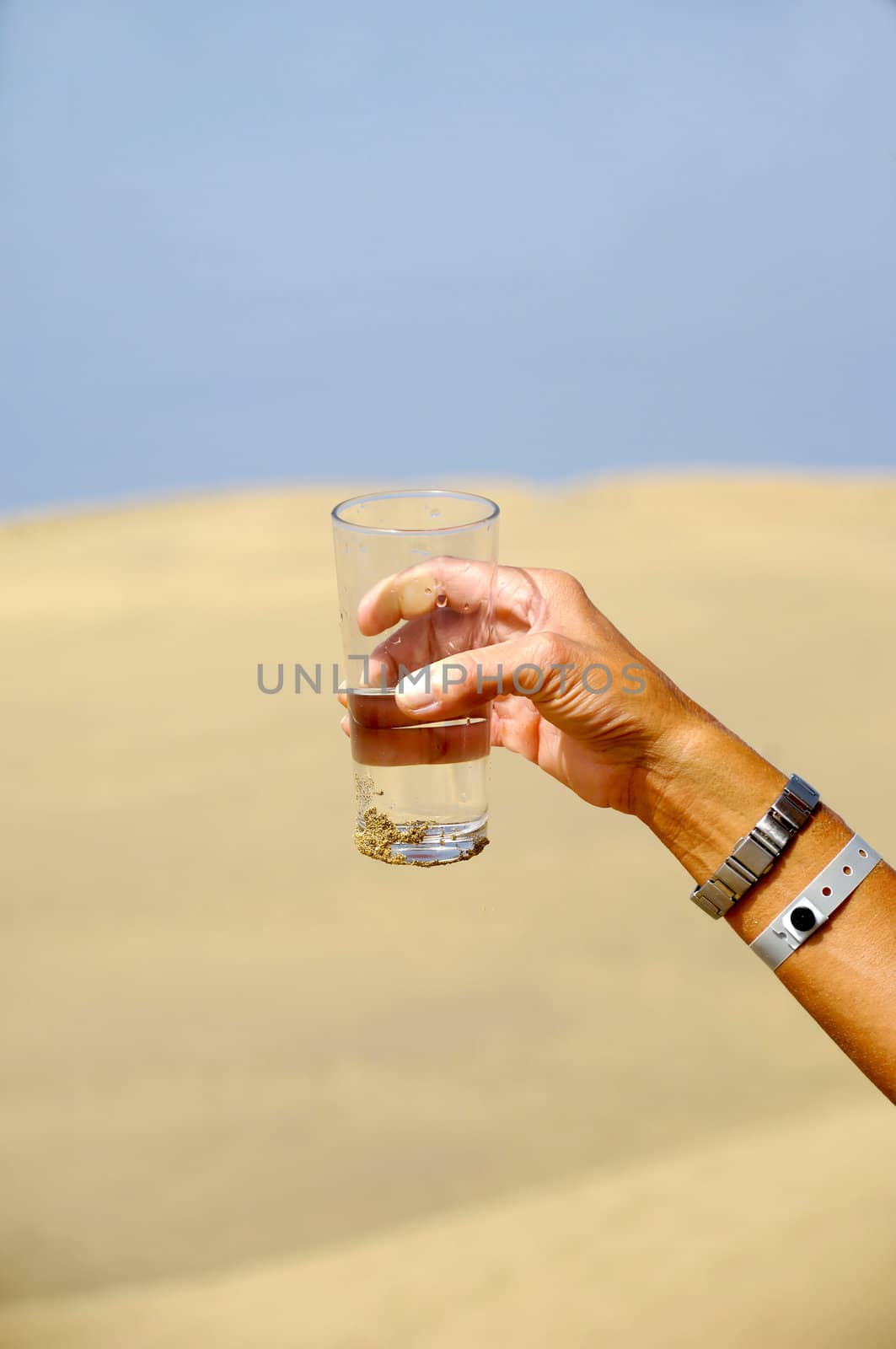 Hand is holding a fresh glass of cold water in desert.