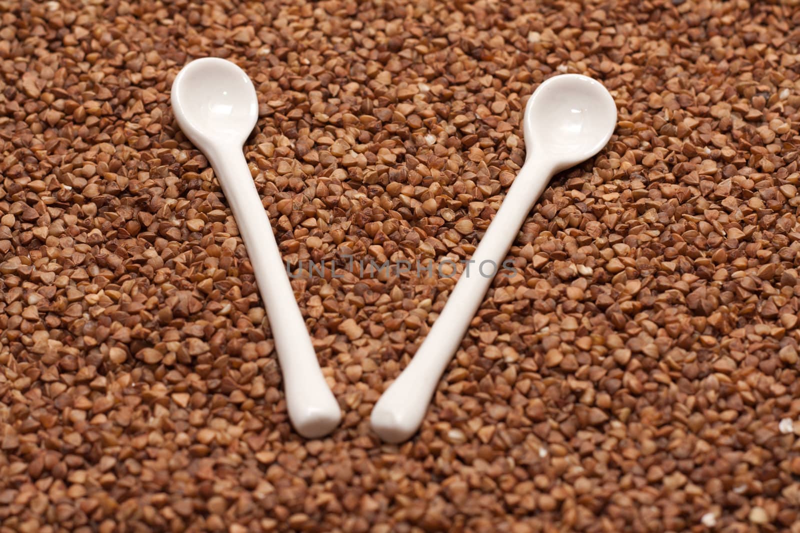 Two ceramic spoons on background from buckwheat
