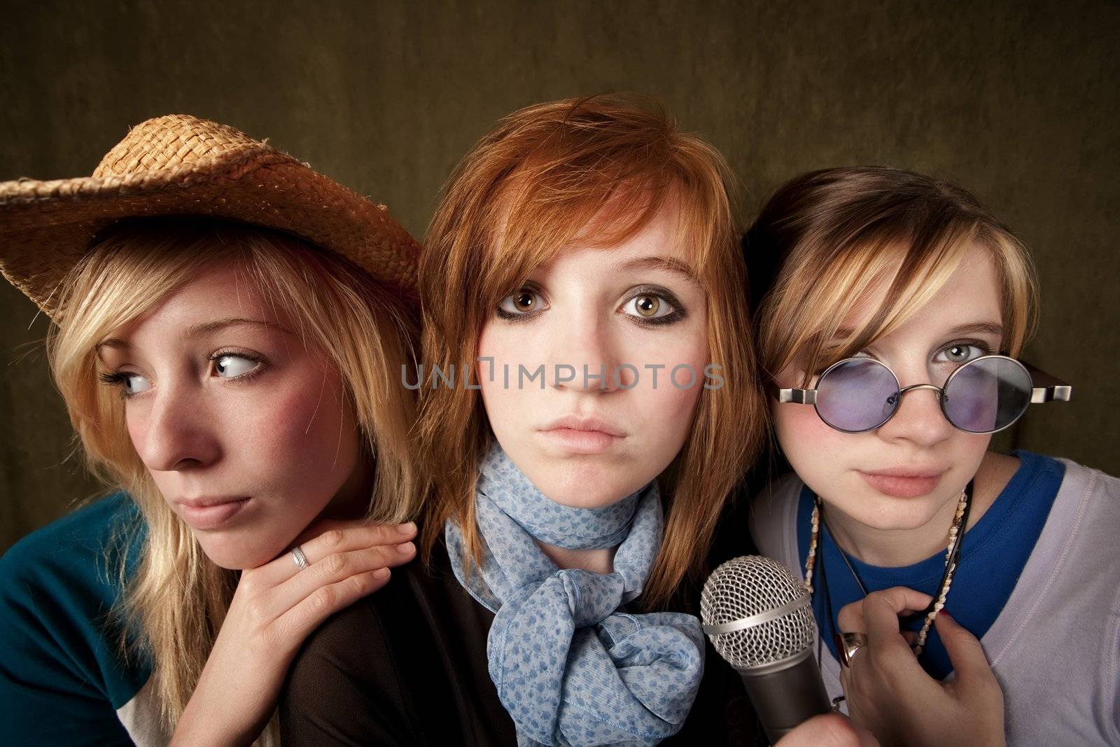 Portrait of three pretty young girls with a microphone on green background