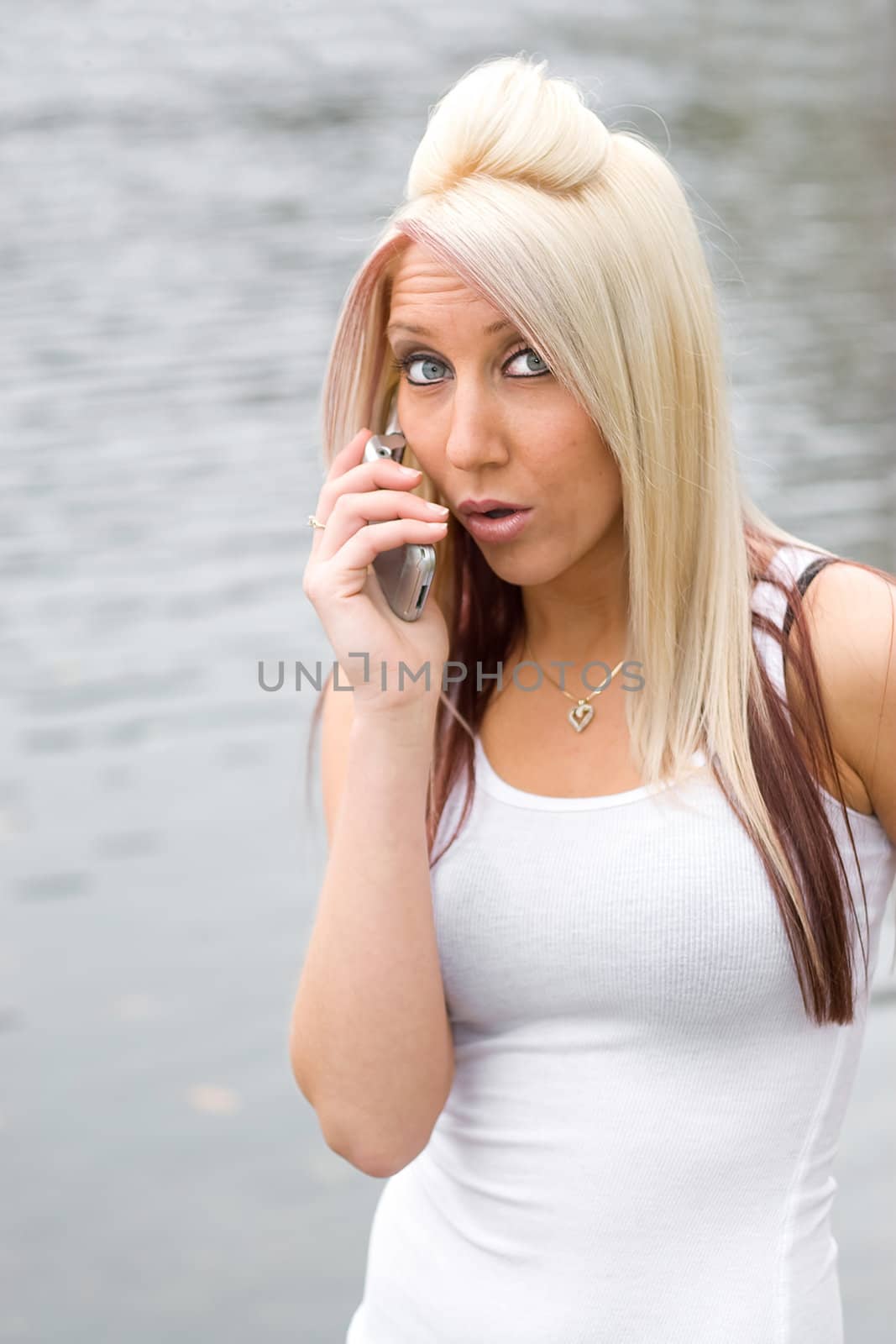 An attractive blonde woman has a surprised look on her face while talking on her cell phone.