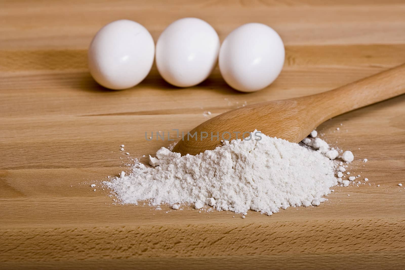 flour and eggs on a wood cutting board with a wooden spoon ready to start baking