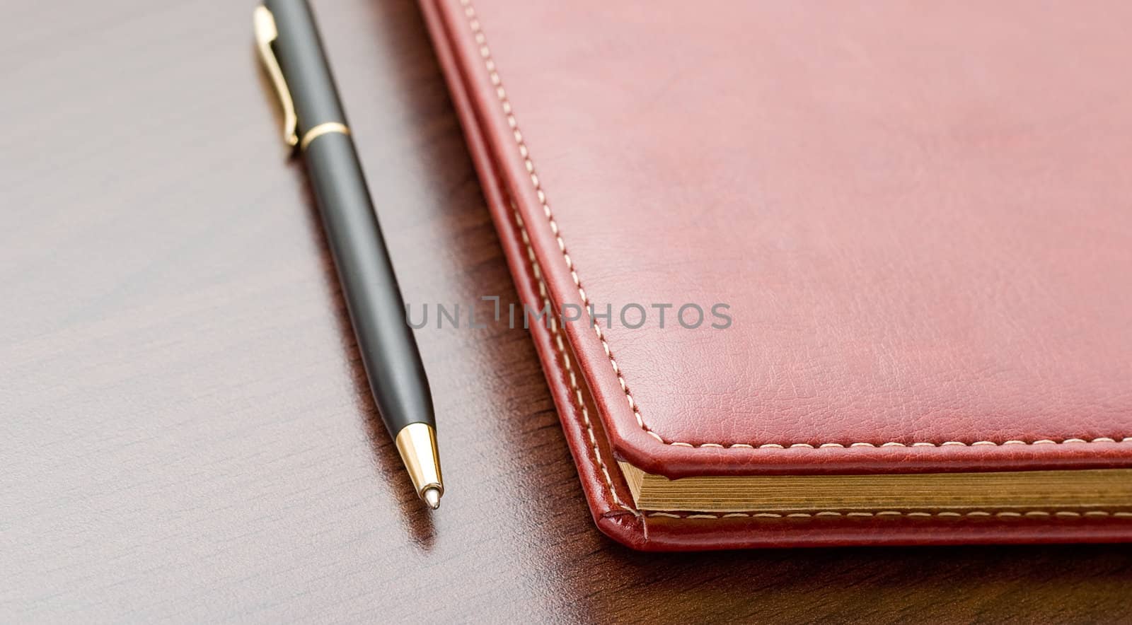 Leather notebook and a black pen on a dark desktop.