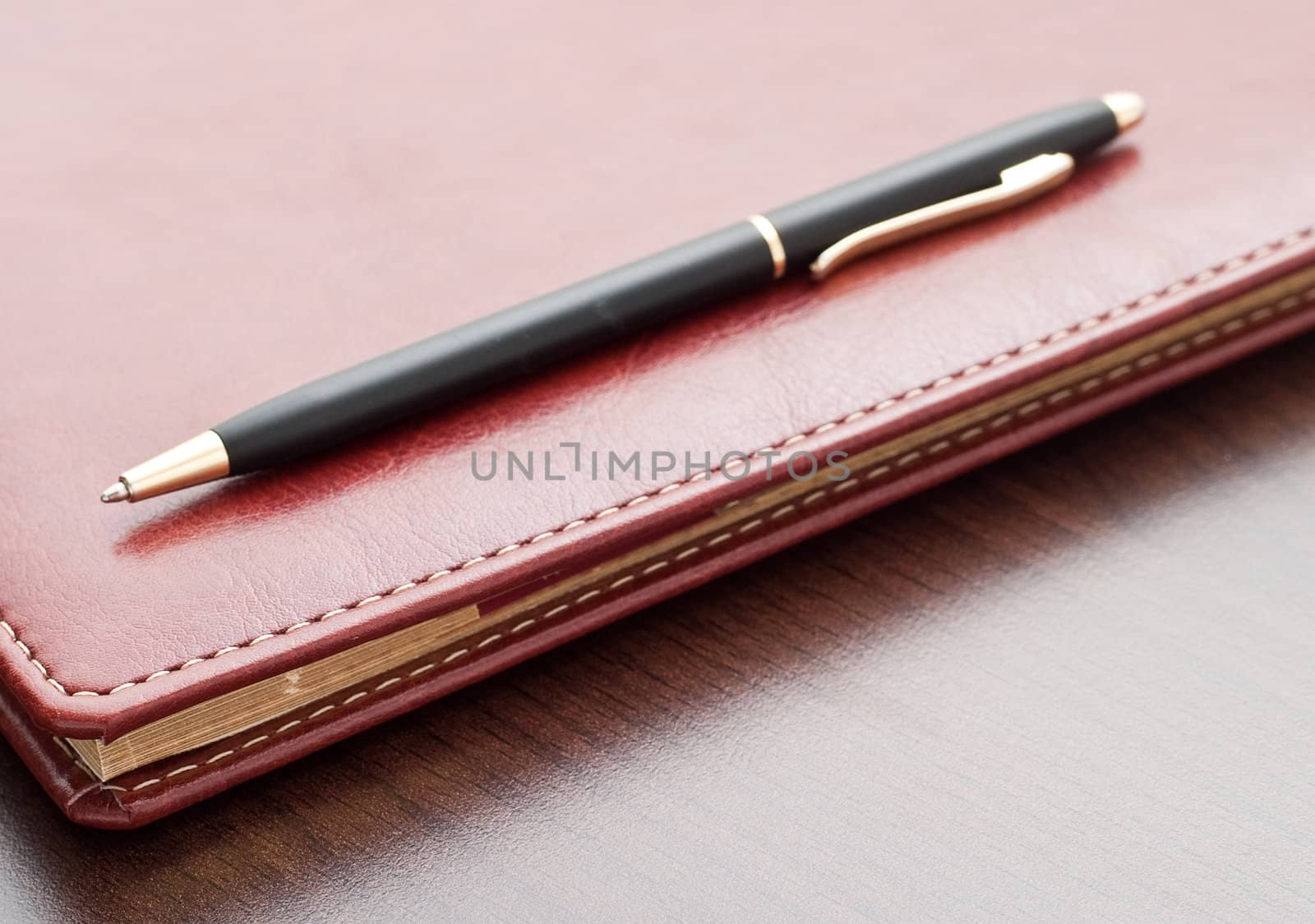 Leather notebook and a black pen on a dark desktop.