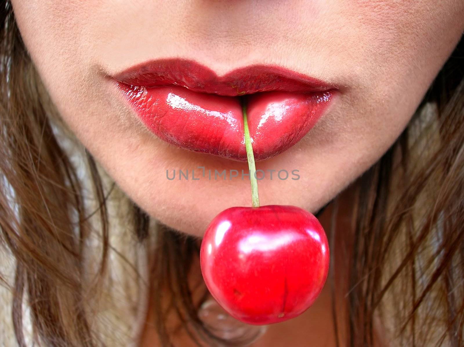 large red cherry in red female lips close up