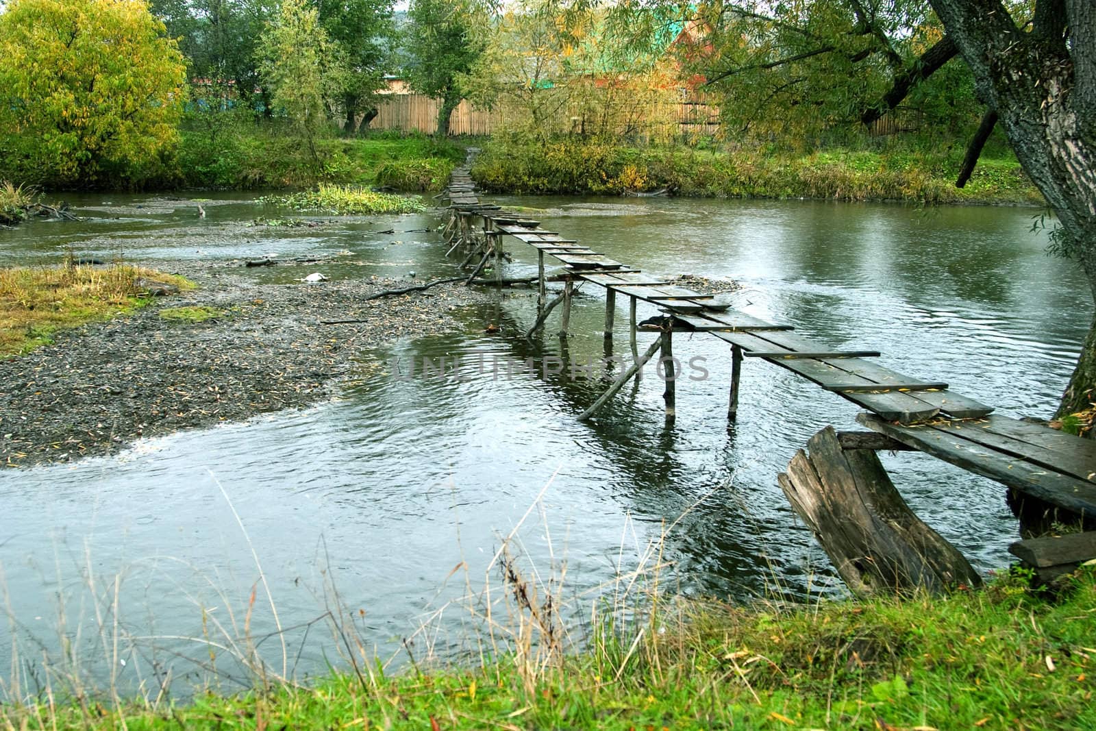 Autumn landscape: the river and the old wooden footbridge. Gloomy weather