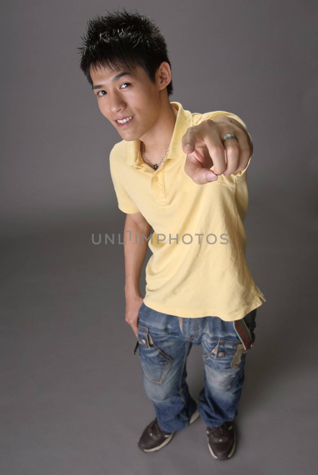 Asian young guy point at you over studio gray background.