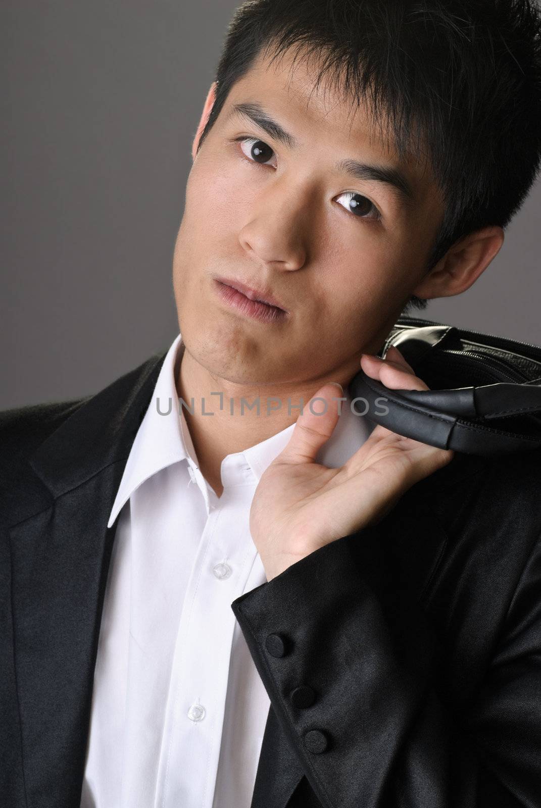 Young attractive business man of Asian holding briefcase on shoulder and looking you.