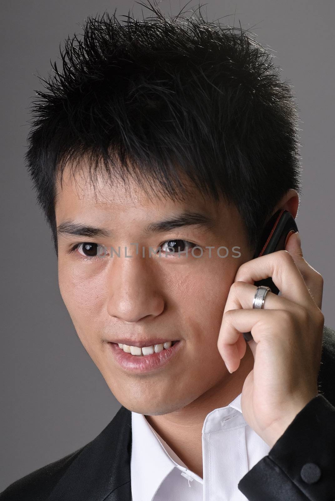Asian business man using cellphone and smiling, closeup portrait over studio gray background.