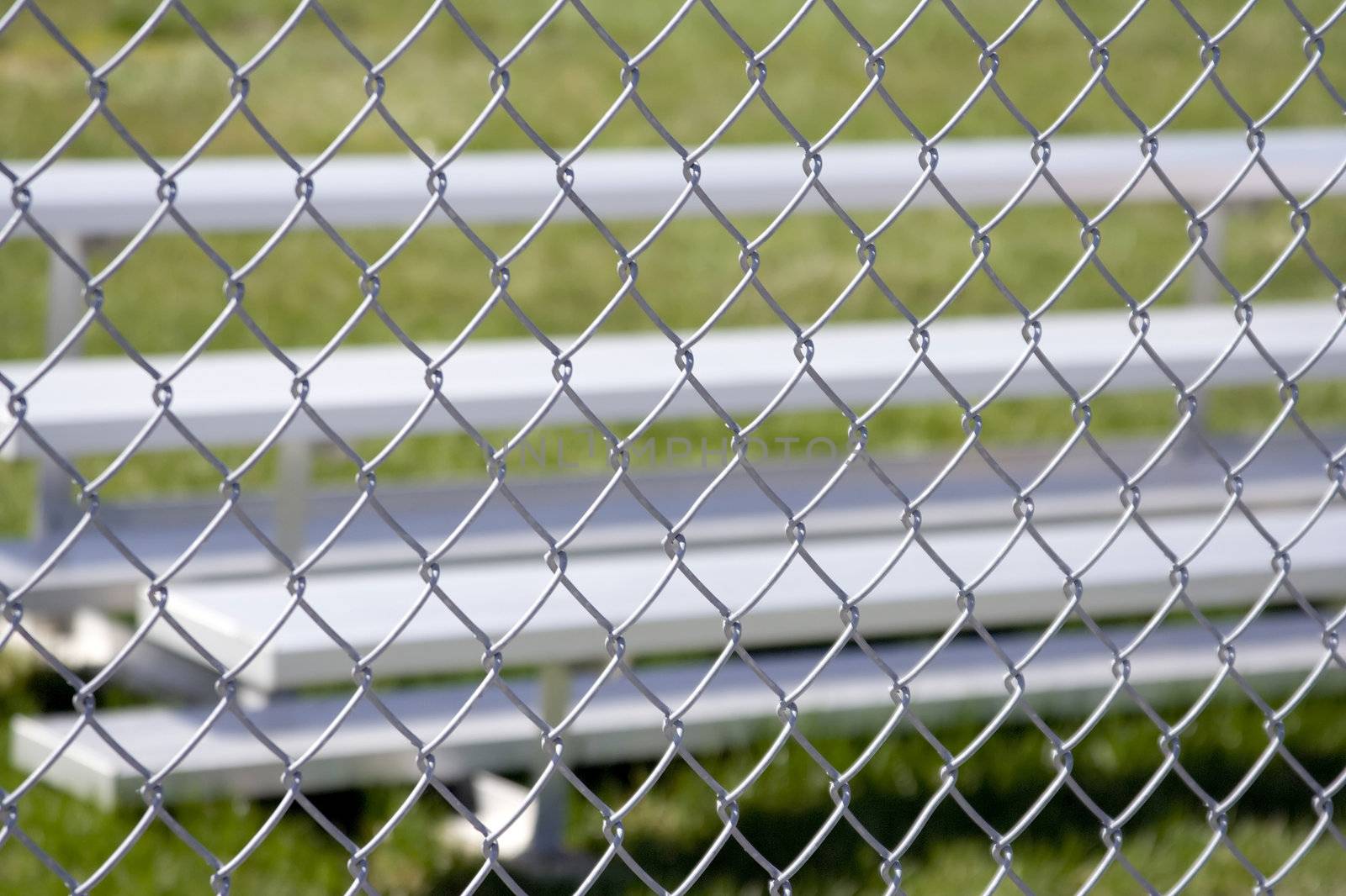 Close up of silver metal sports bleachers shot thru a fence and the fence is in focus the bleachers or blurred 