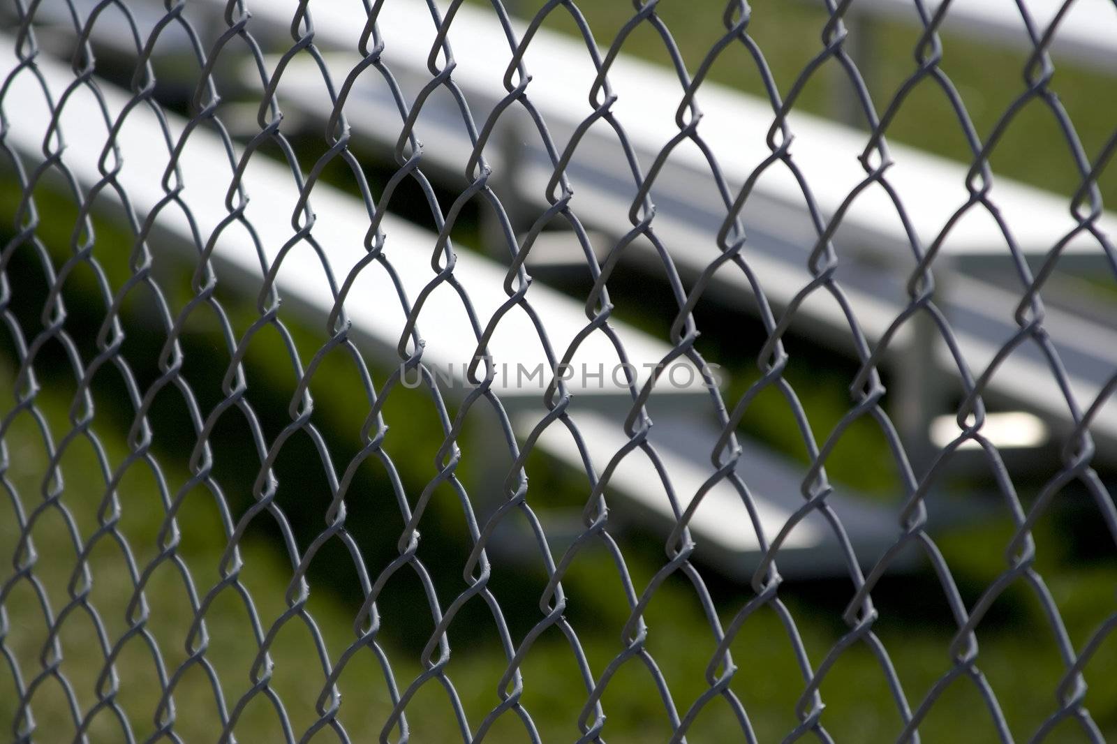 Close up of silver metal sports bleachers shot thru a fence and the fence is in focus the bleachers or blurred 