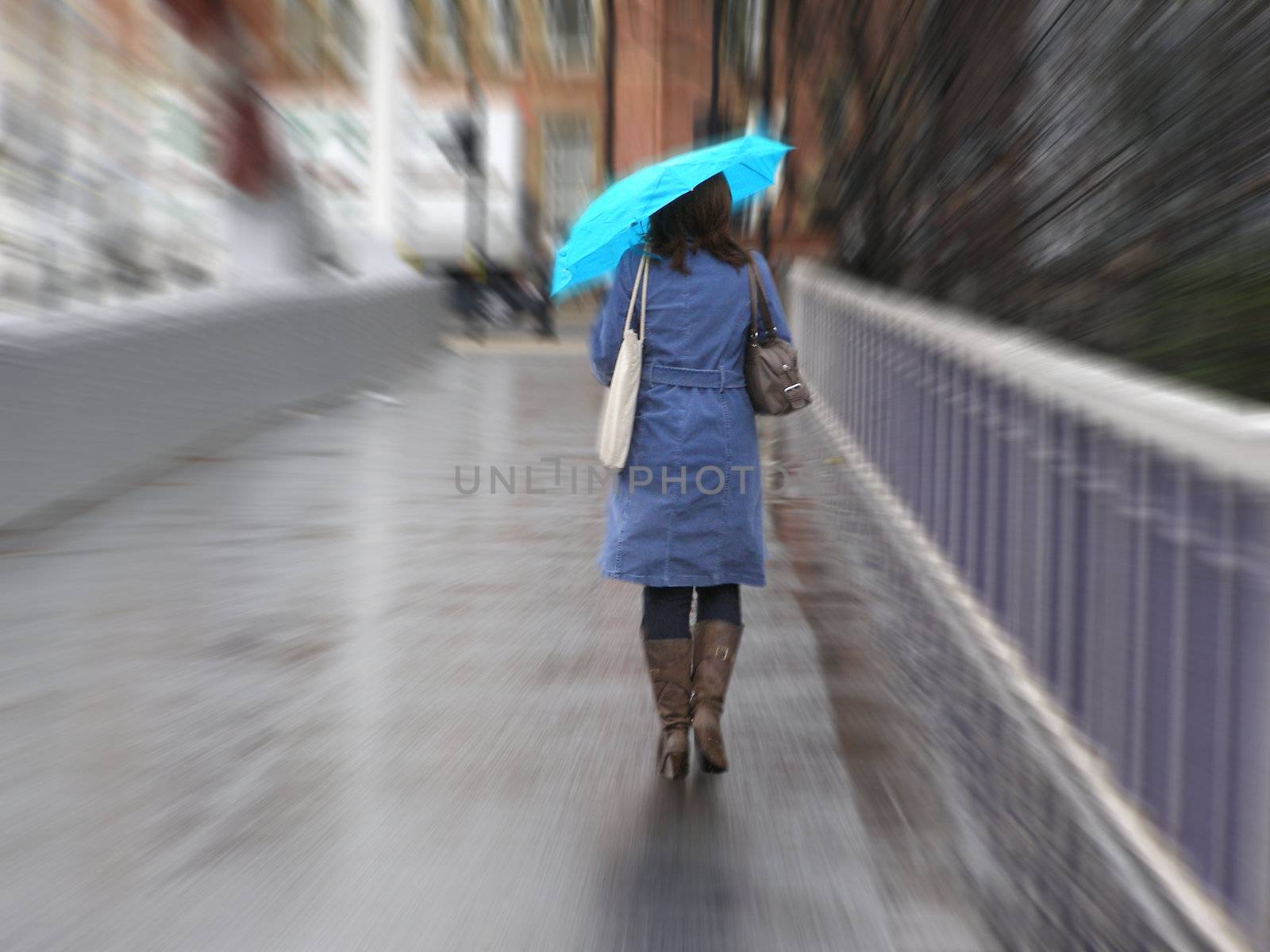 Girl walking in the rain with umbrella, dressed in a blue mac with an azure umbrella