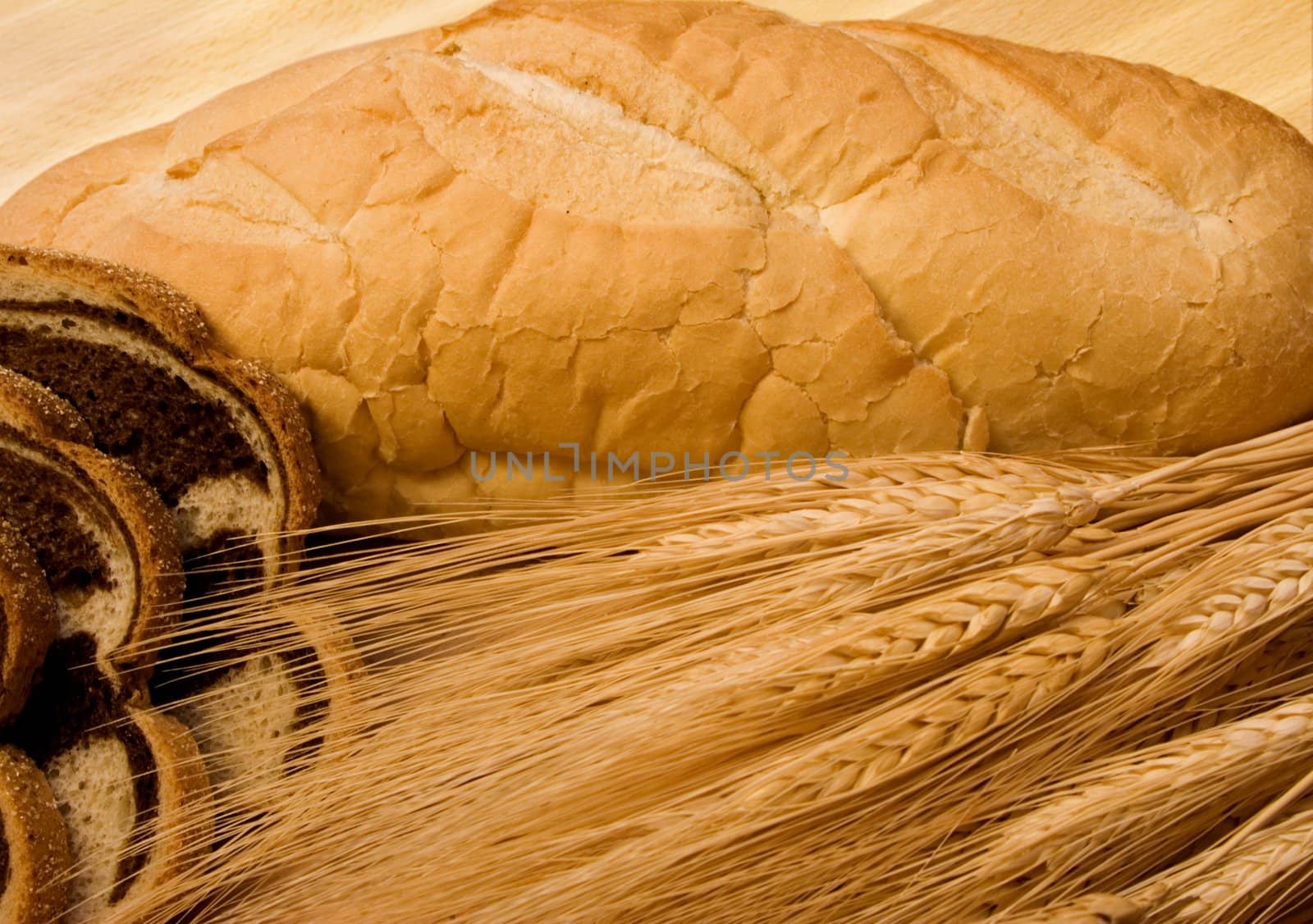 close up of two different kinds of bread and some wheat on a wood cutting board