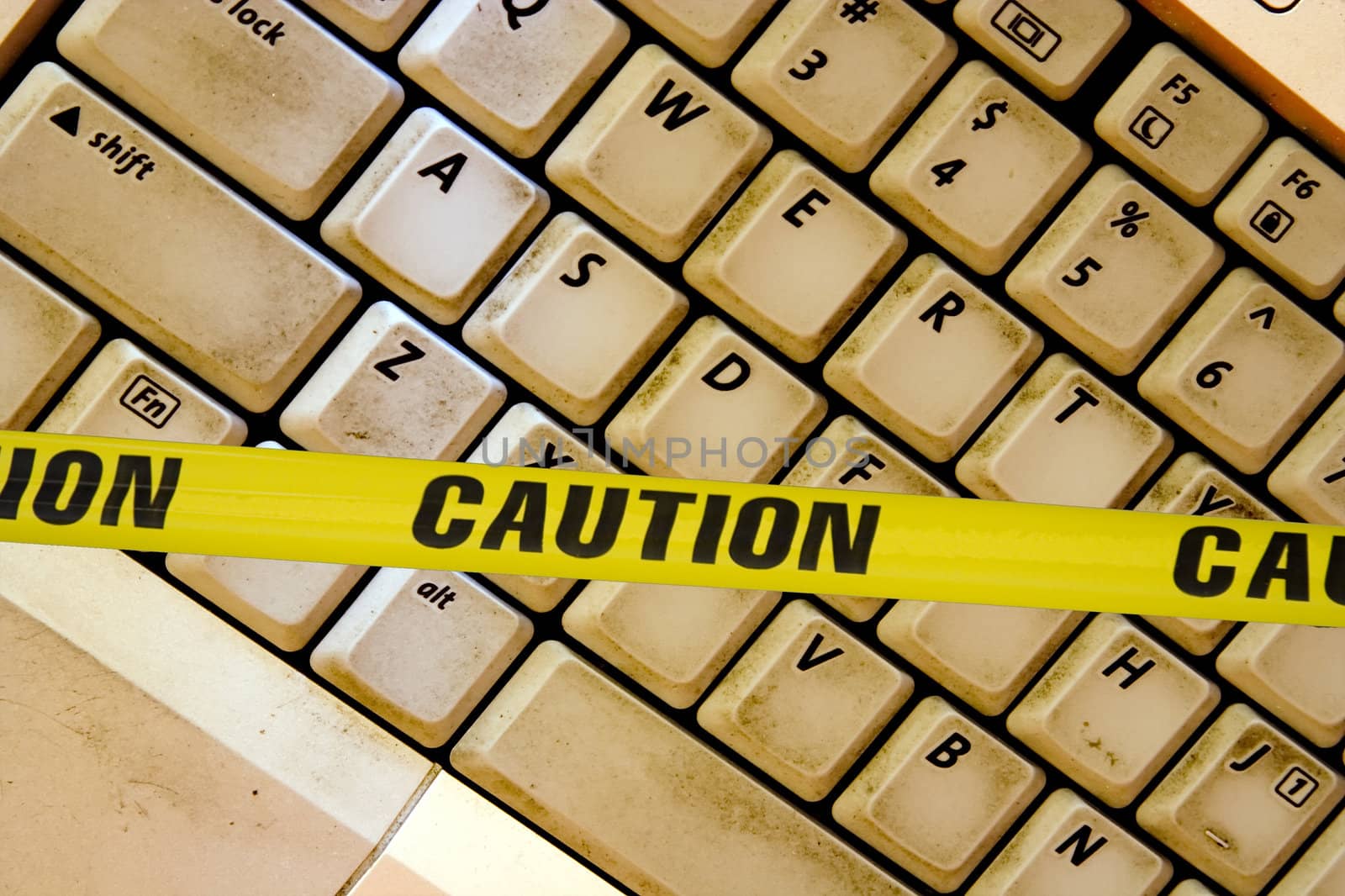 concept of warning of the bad things online caution tape acrossed a dirty laptop keyboard