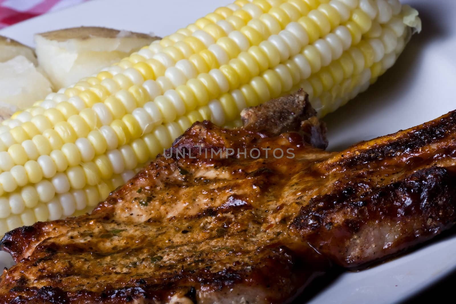 country style dinner corn on the cob on a white plate with a red checkered place mat