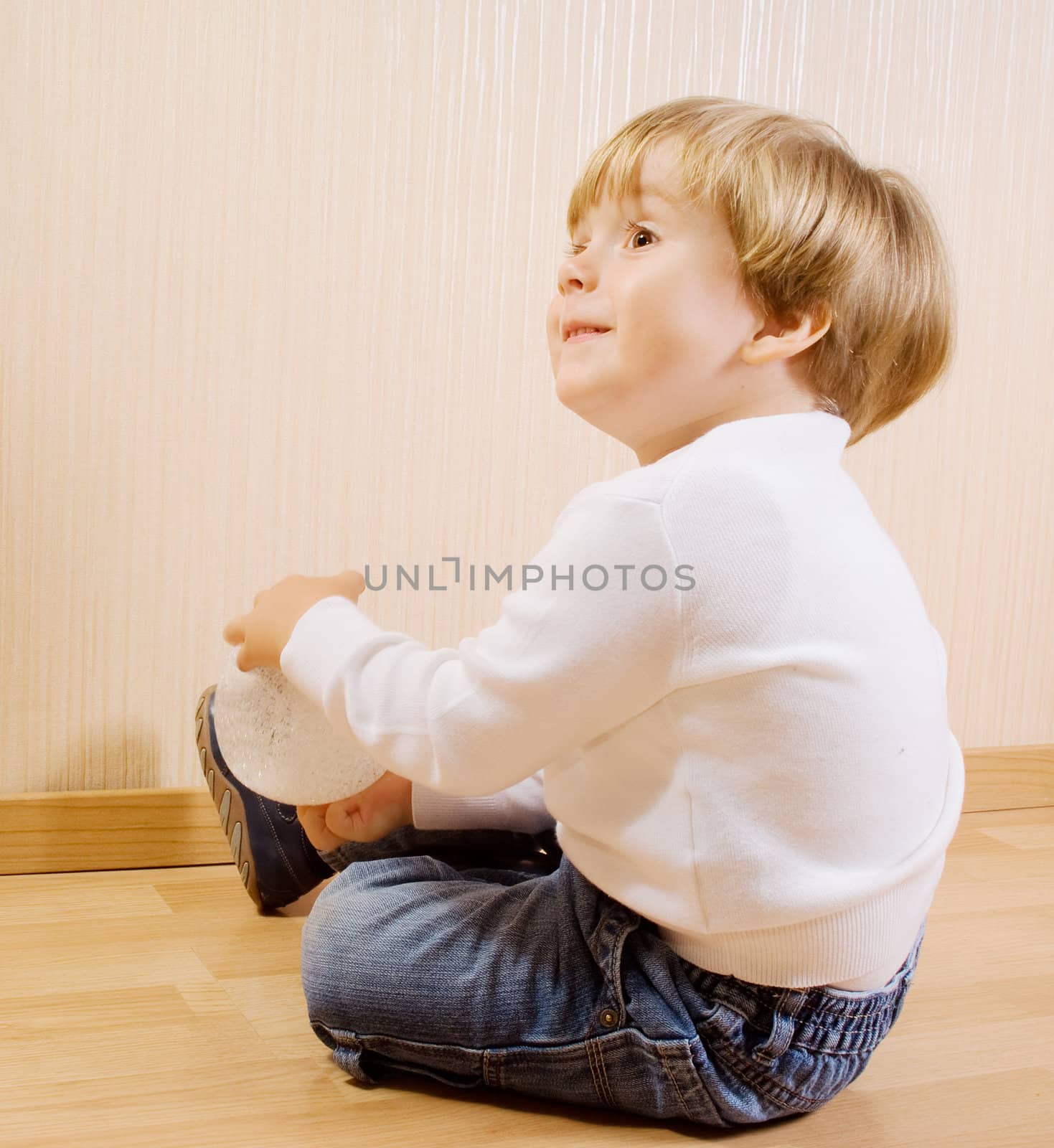 The child playing on the wood floor with white ball