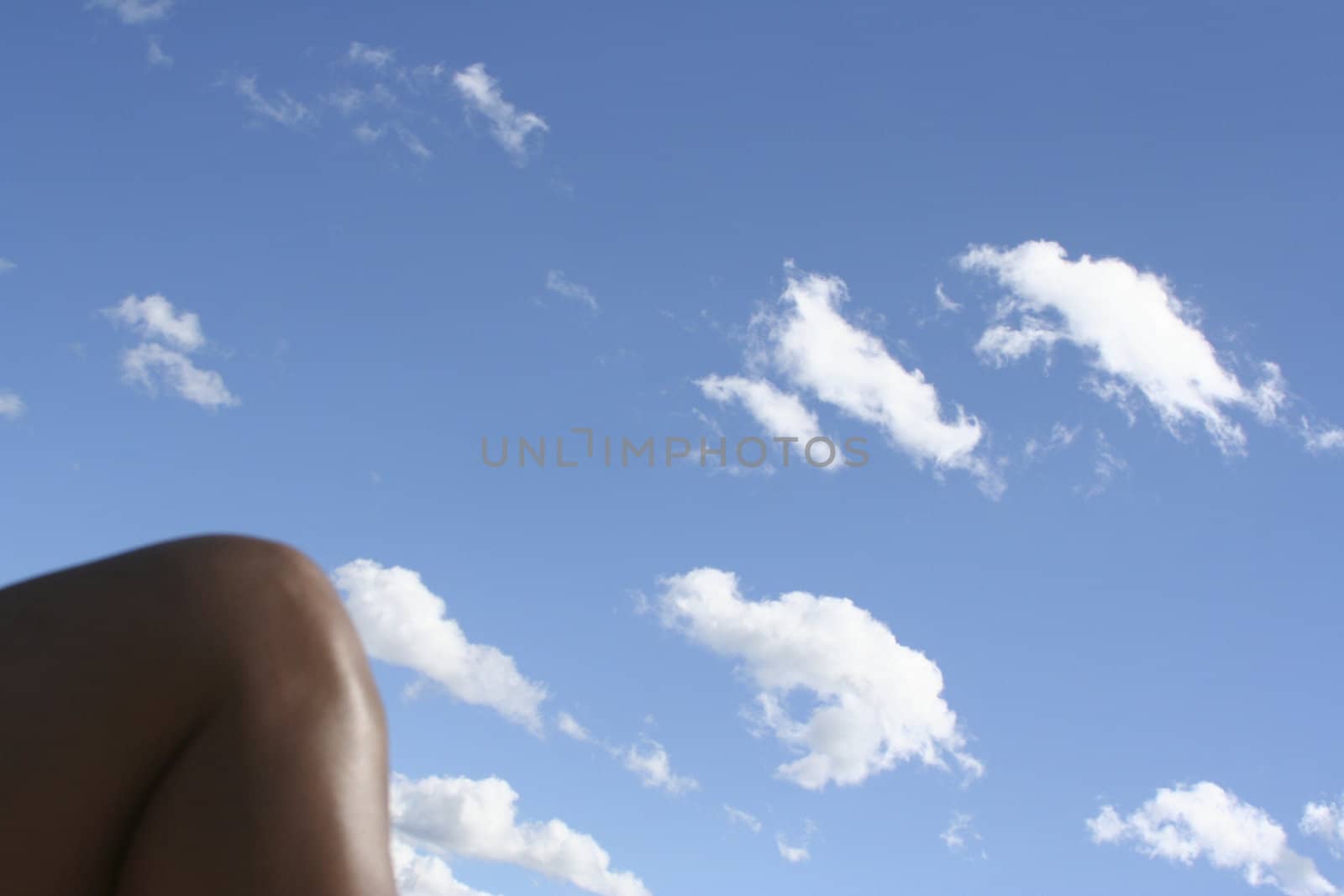 Womens knee against a blue sky with white puffy clouds