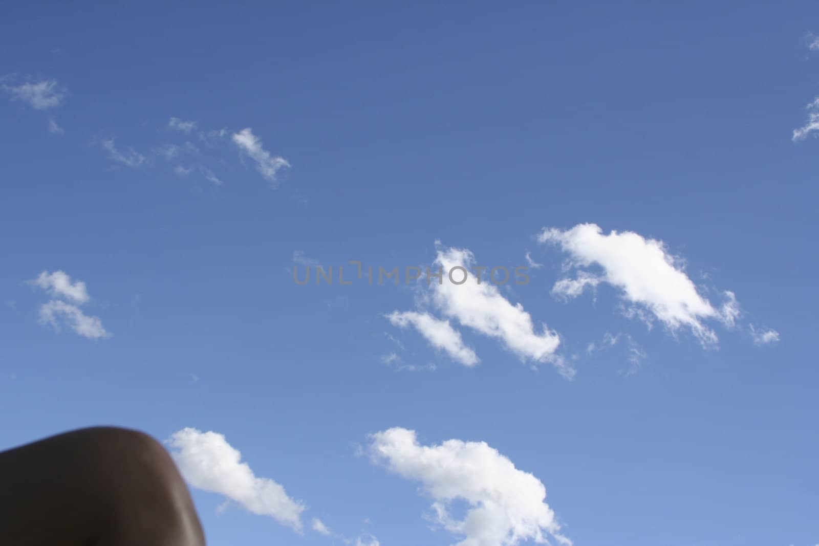 Womens knee against a blue sky with white puffy clouds