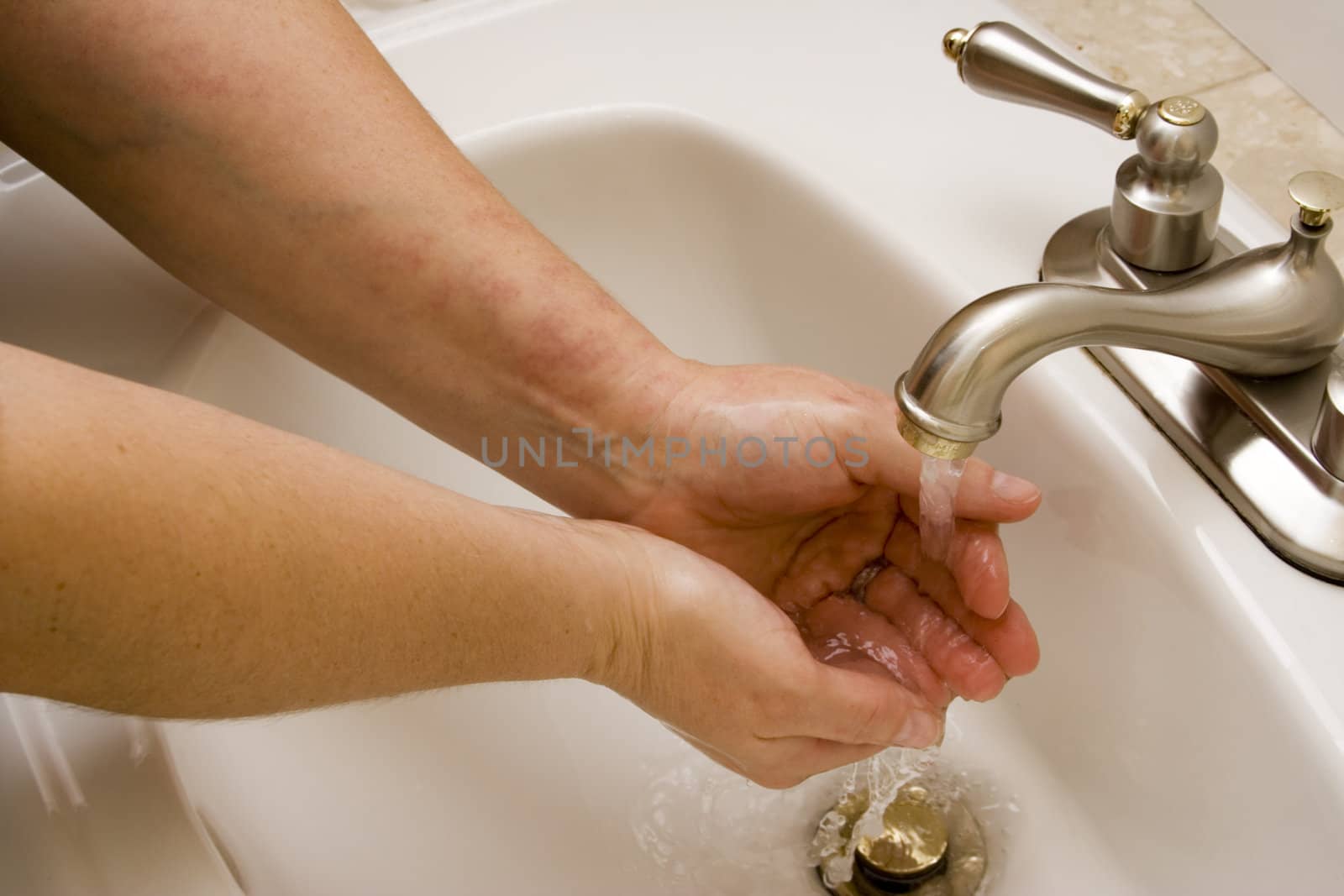 woman washing hand under running water white sink chrome spout