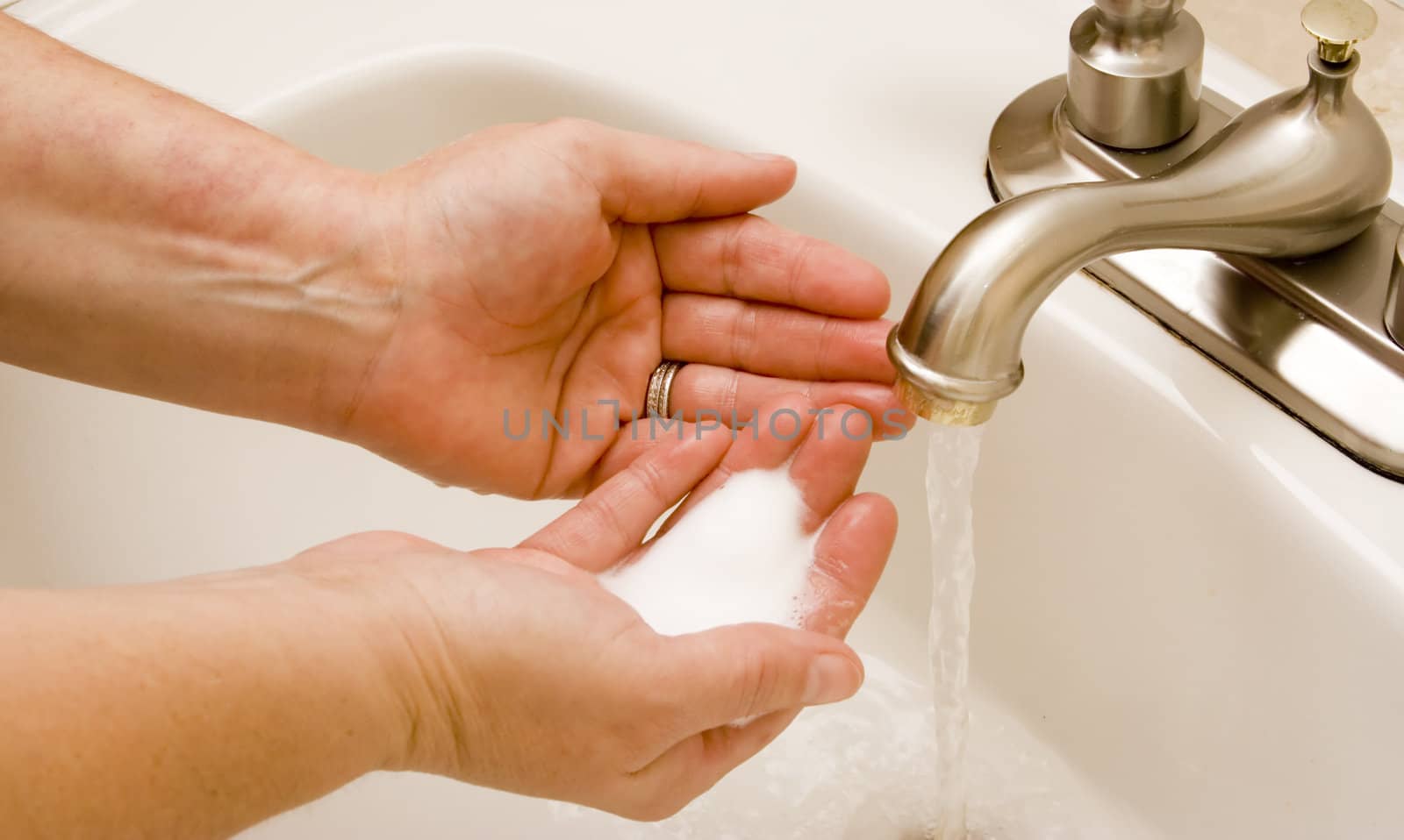 woman washing hand under running water white sink chrome spout