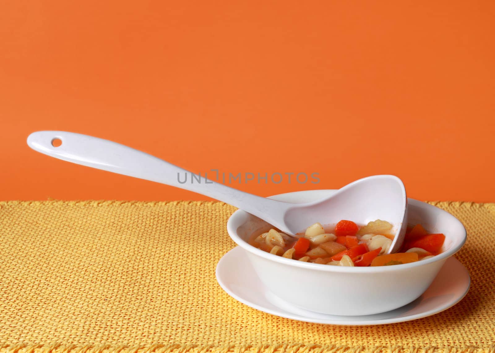 vegetable soup in white bowl, yellow tablecloth and oragne background