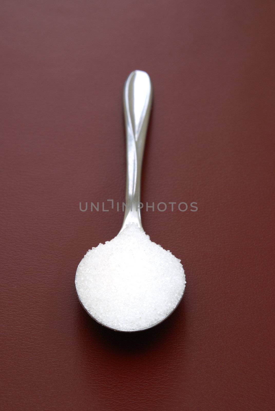 A teaspoon of sugar on red background.