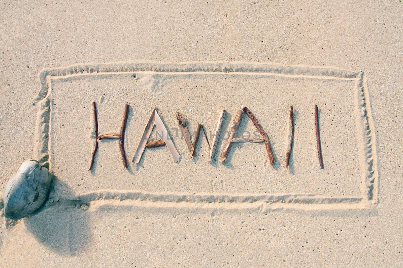 Hawaii written with sticks on a sandy beach with coconut