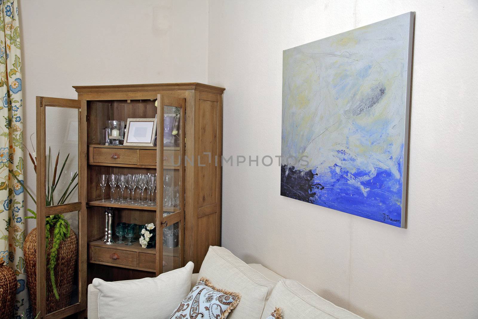 A living room with a couch, a cupboard, and a painting on the wall
