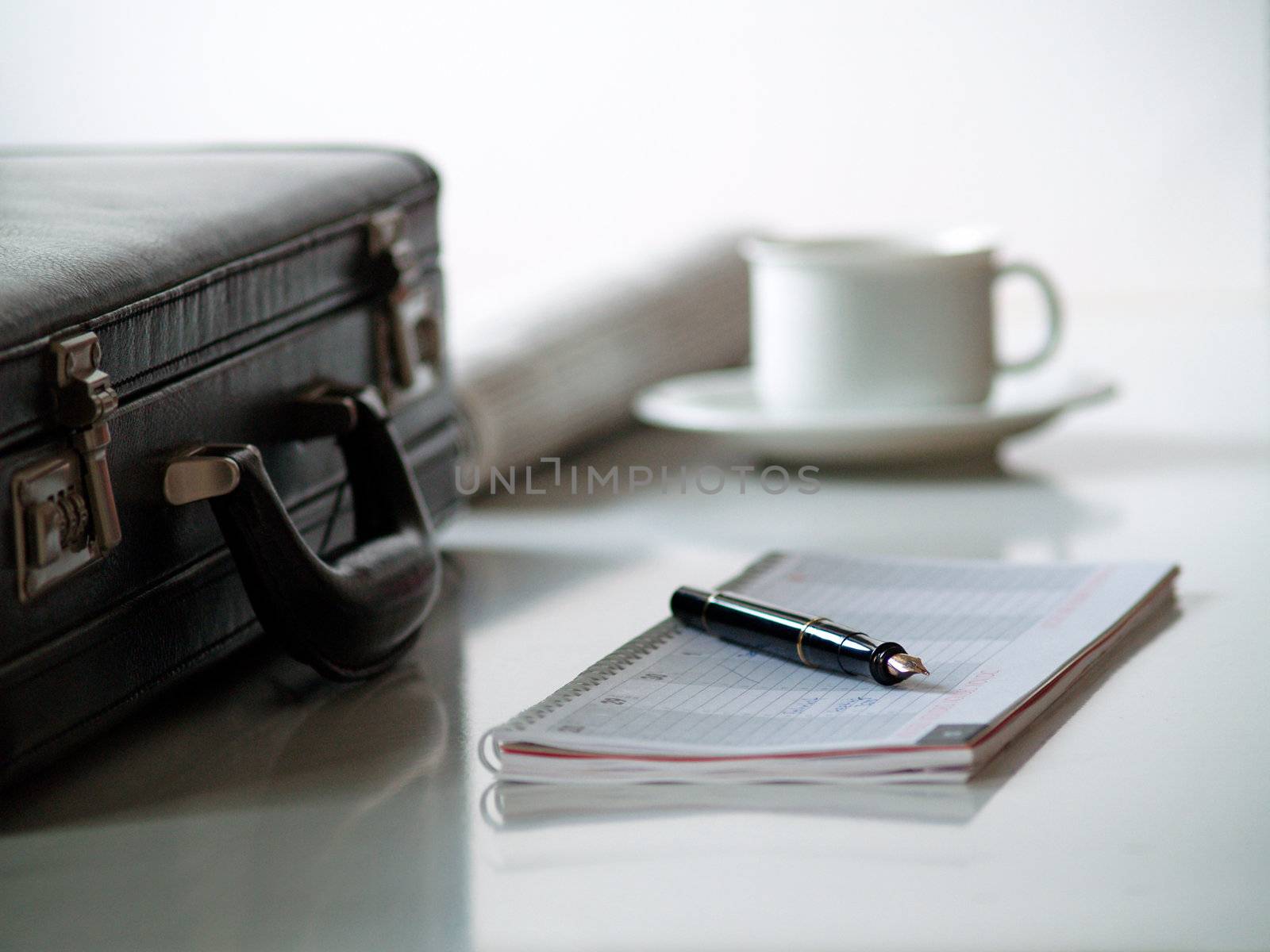 A suitcase, a calender with a pen on top, and a cup of coffee and a paper
