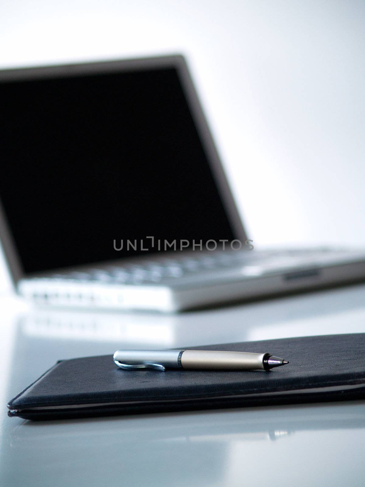 A black leather folder with a pen on top and a laptop in the background

