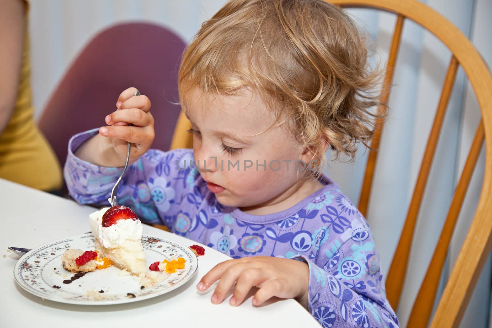Cute little European toddler girl enjoying a piece of birthday cake.