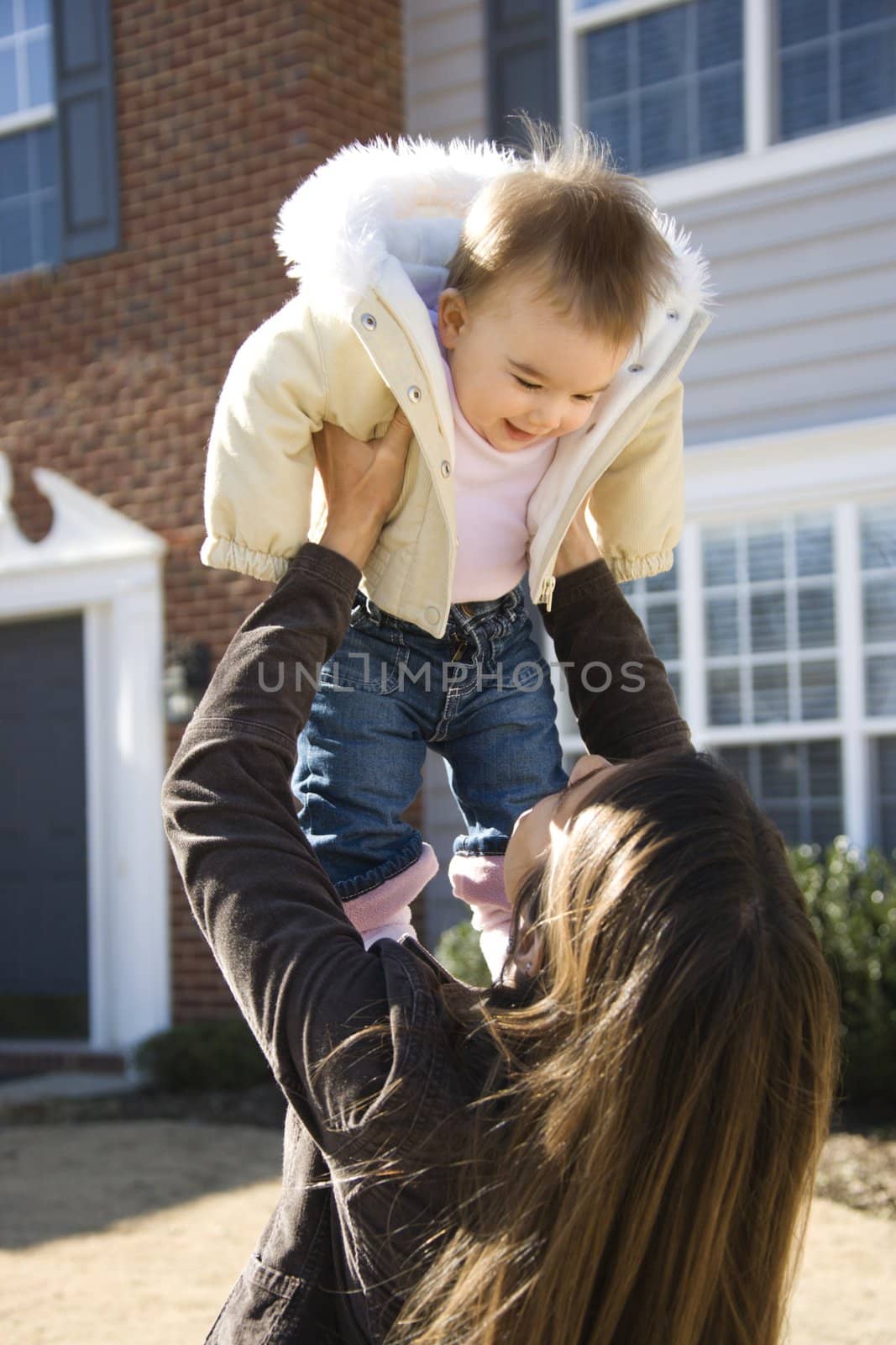 Caucasian mother holding up baby girl in front of house outside.