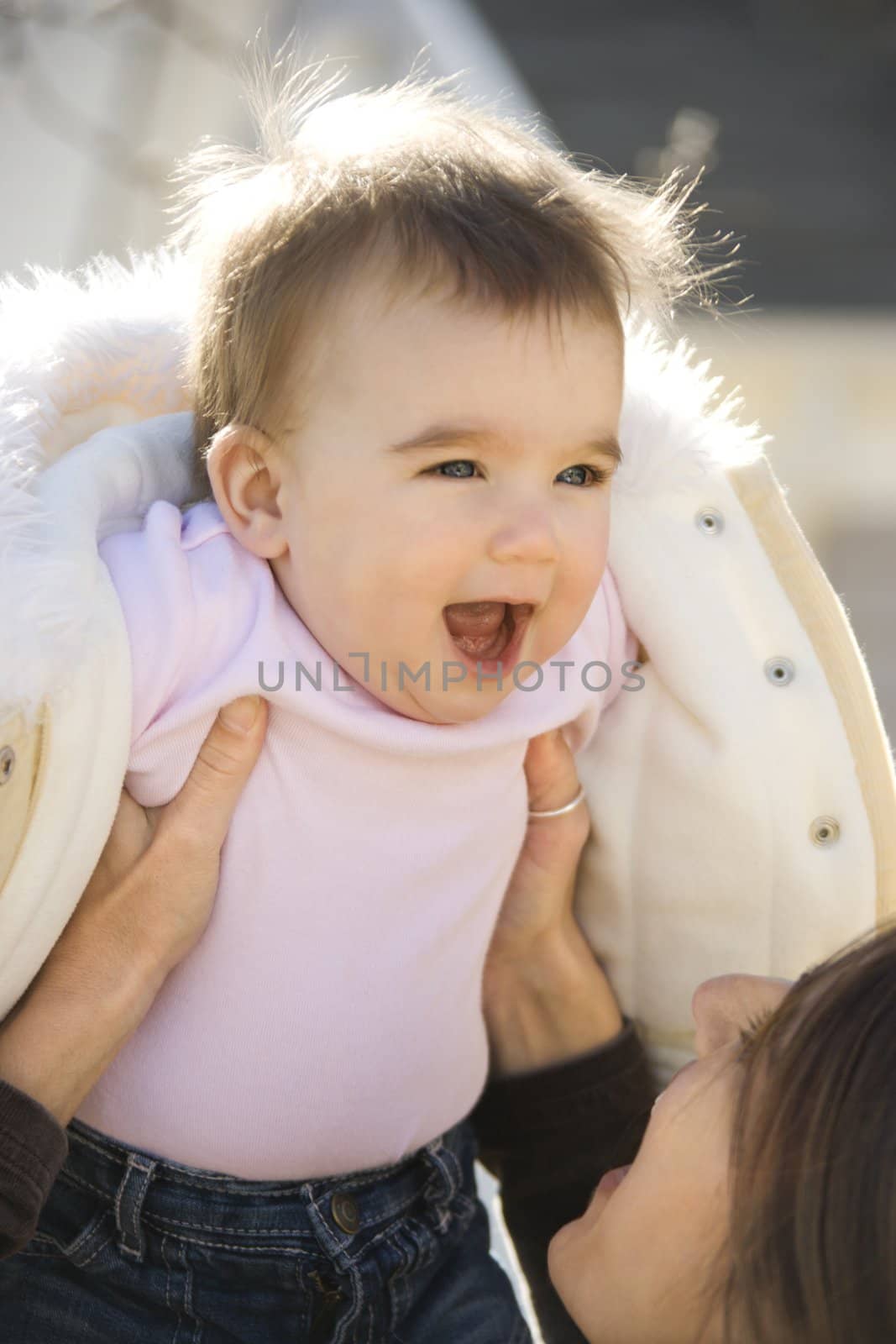 Caucasian mother holding up smiling baby girl.