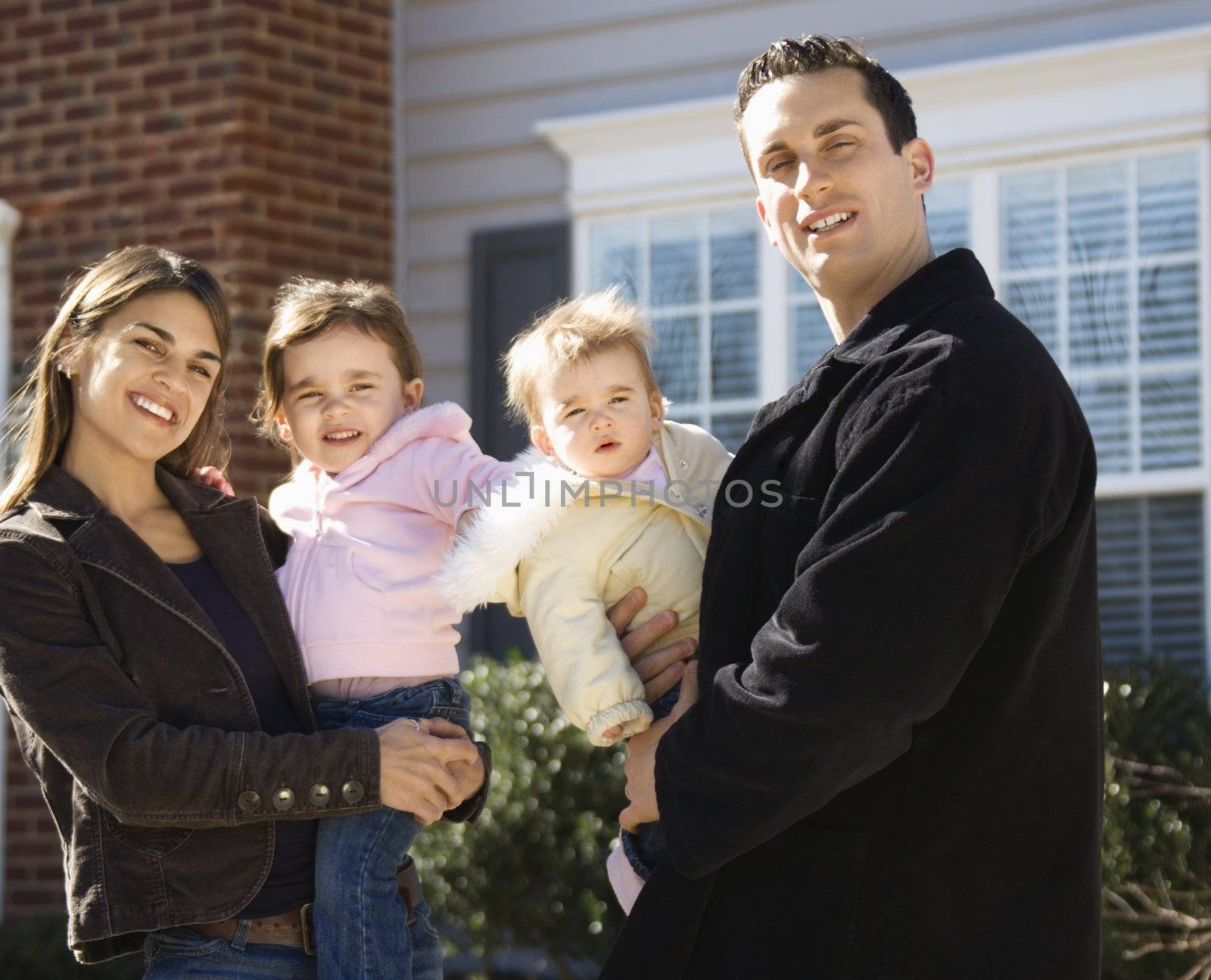 Caucasian mother and father with children standing in front of house.