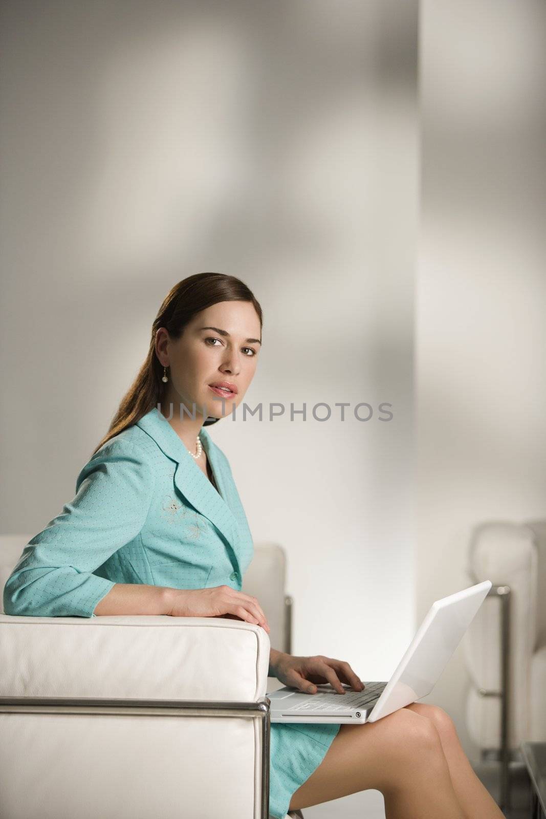 Caucasian mid adult professional business woman sitting in modern office working on laptop computer.