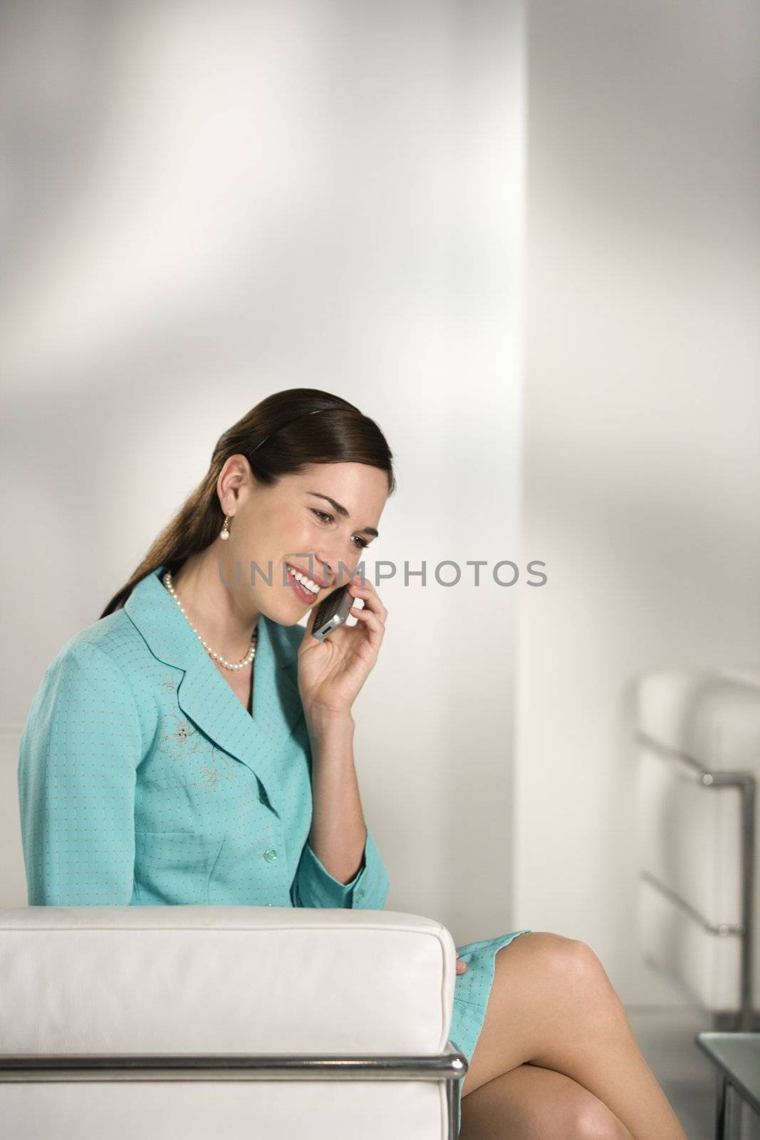 Caucasian mid adult professional business woman sitting in modern office talking on cell phone and smiling.