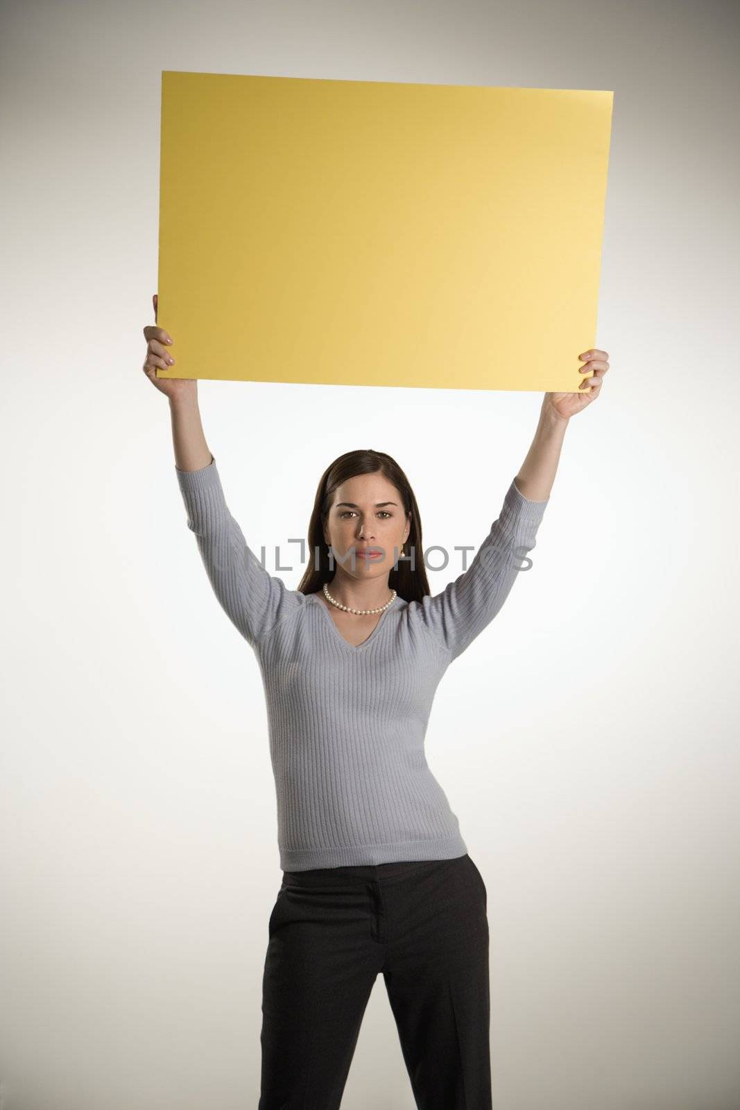 Caucasian mid adult professional business woman standing holding up blank yellow sign above her head.