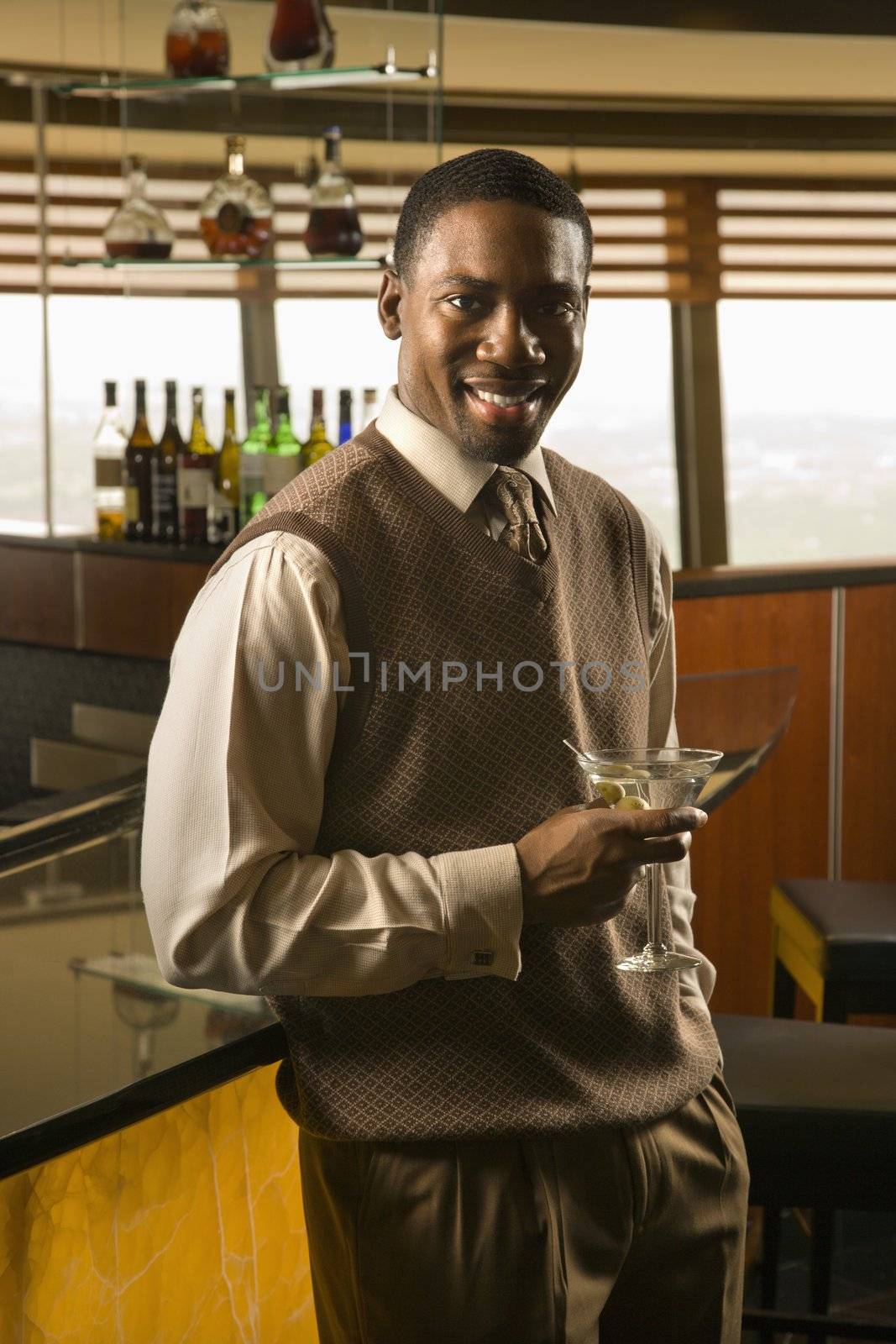 African American mid adult man at bar with martini smiling at viewer.