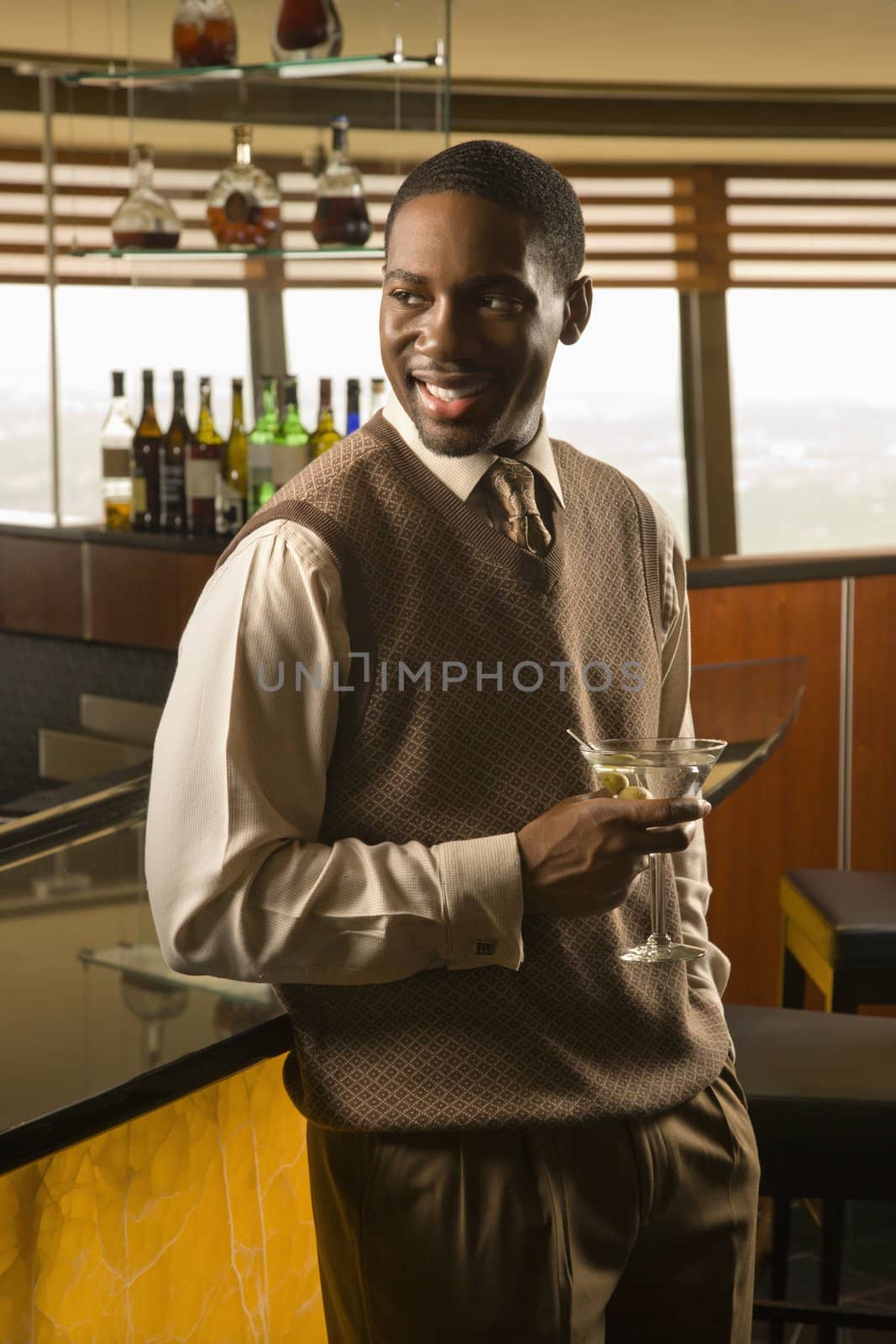 African American mid adult man standing at bar with martini.