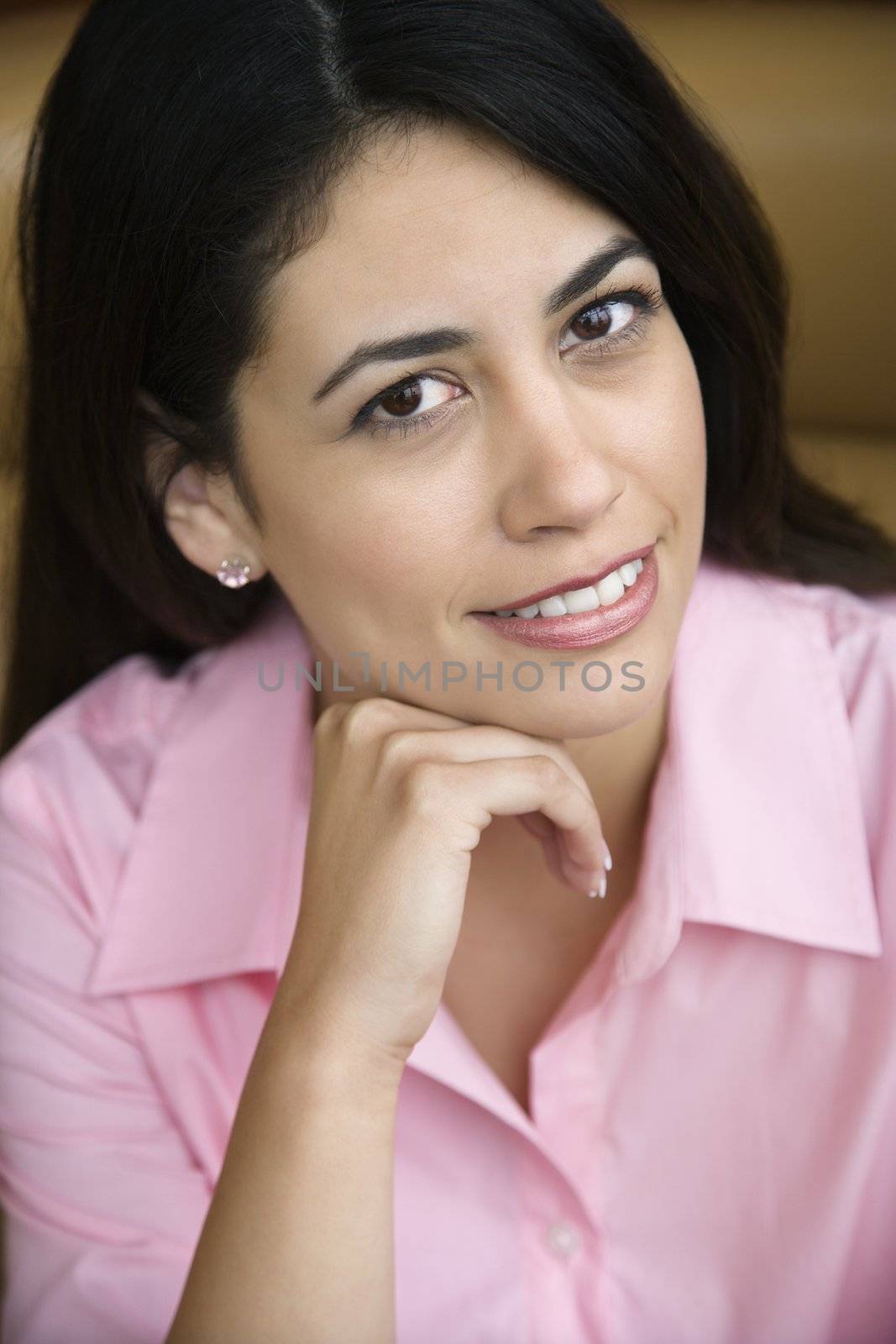 Mid adult Hispanic woman smiling at viewer with hand to head.