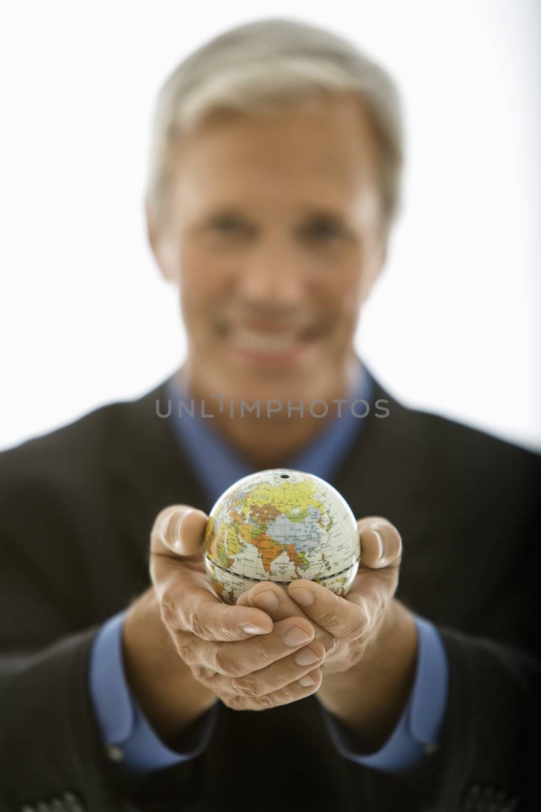 Selective focus of Caucasian middle aged businessman smiling and holding globe towards viewer.