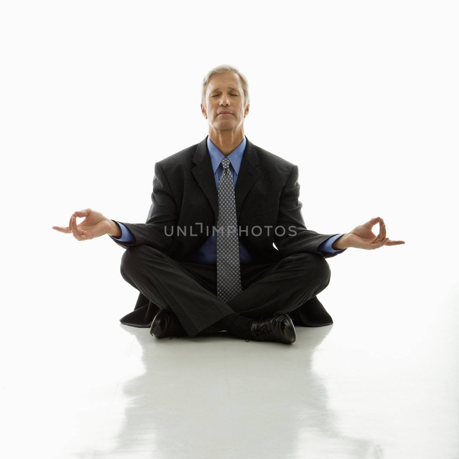 Caucasian middle aged businessman meditating in yoga lotus pose on floor.