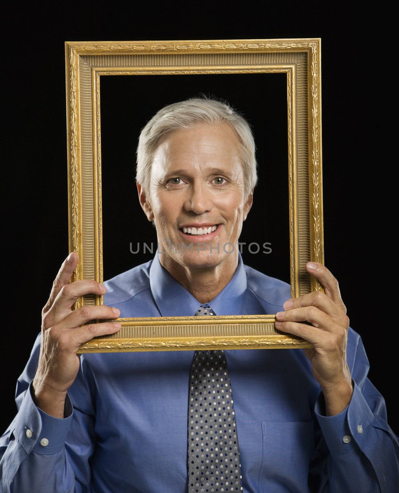 Caucasian middle aged businessman smiling through empty picture frame in front of face.