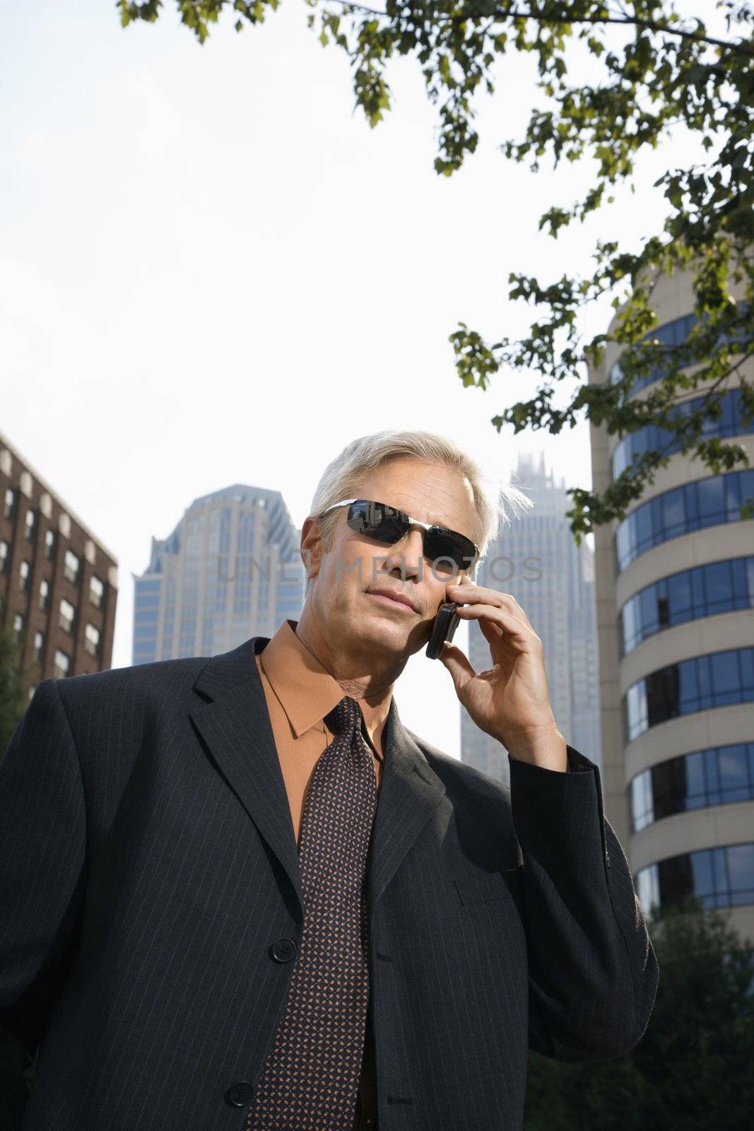 Caucasian middle aged businessman in sunglasses talking outdoors on cell phone.