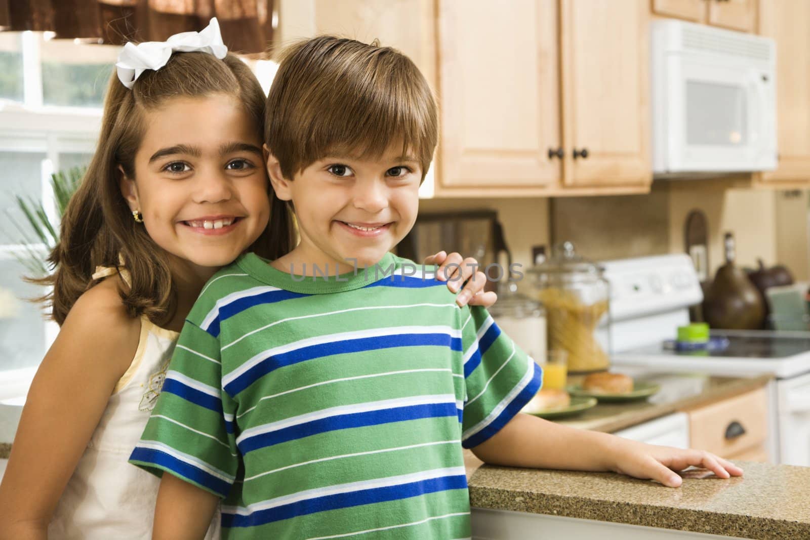 Hispanic children in kitchen smiling at viewer.