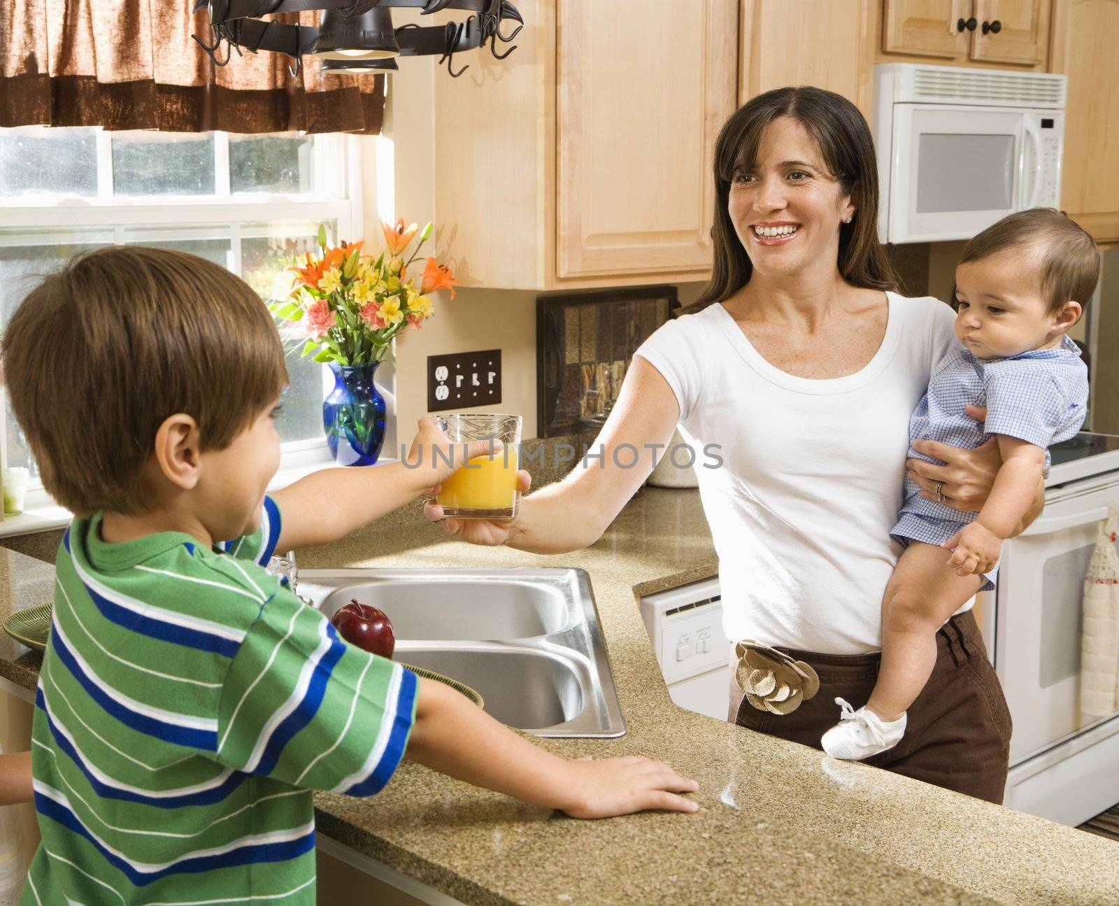 Hispanic mother and children in kitchen with juice.