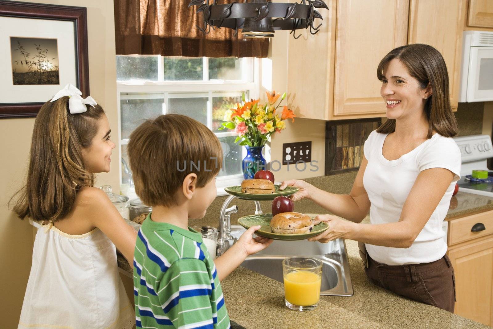 Hispanic mother giving healthy breakfast to young children in home kitchen.