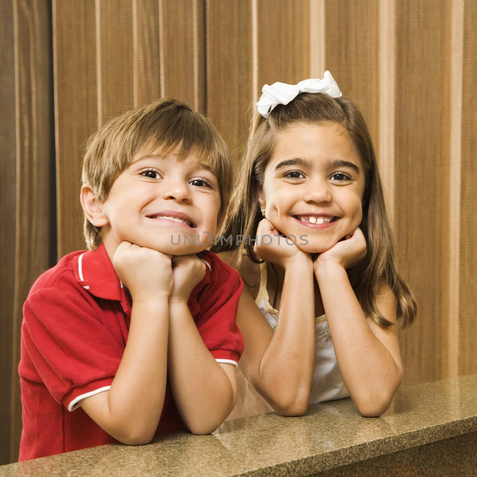 Hispanic children with their head on hands smiling at viewer.