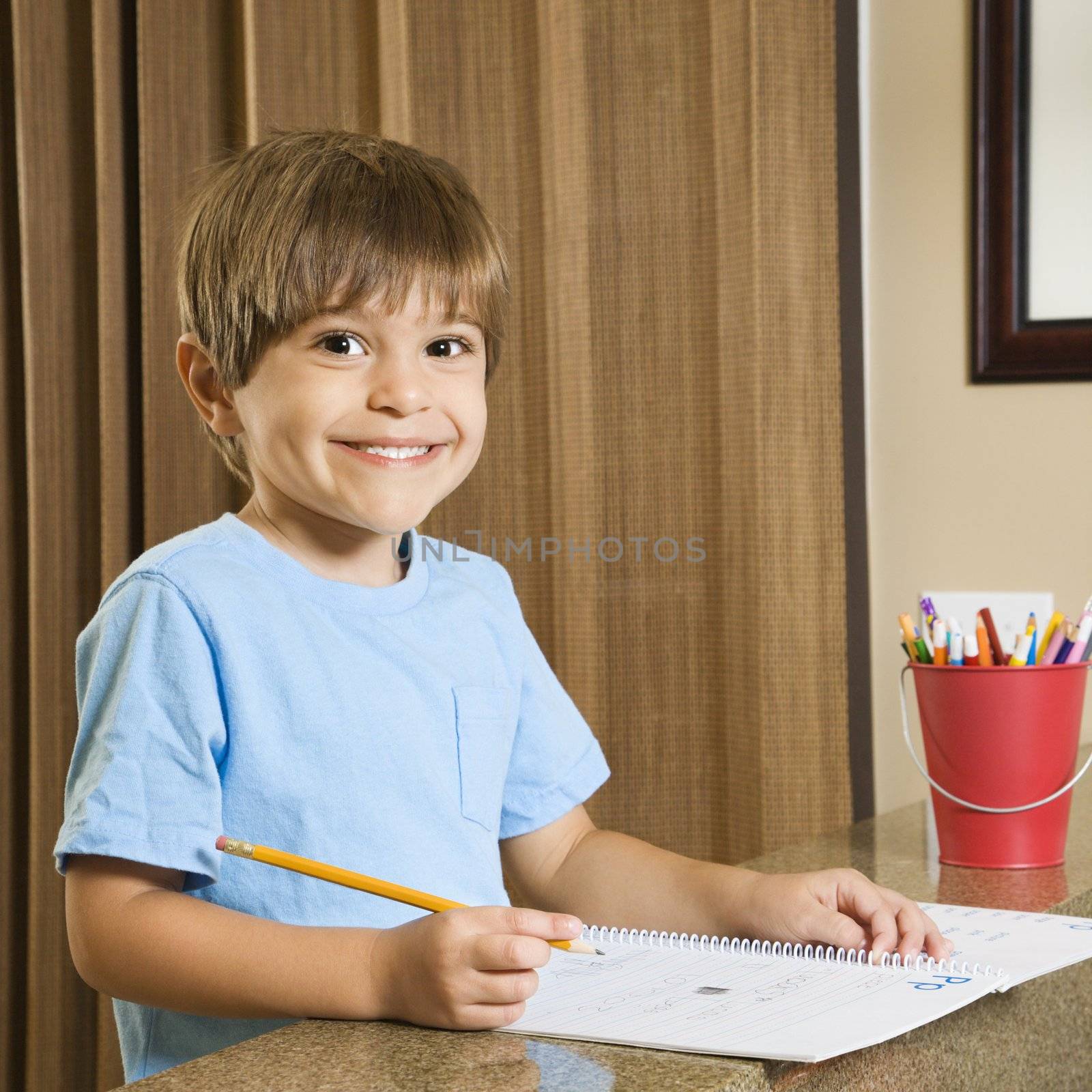 Hispanic boy smiling at viewer and doing homework.