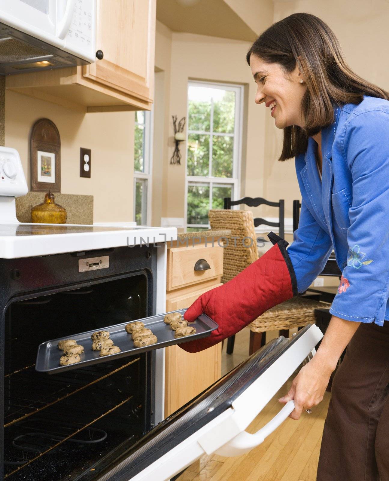 Side view of Hispanic mid adult woman putting cookies into oven.