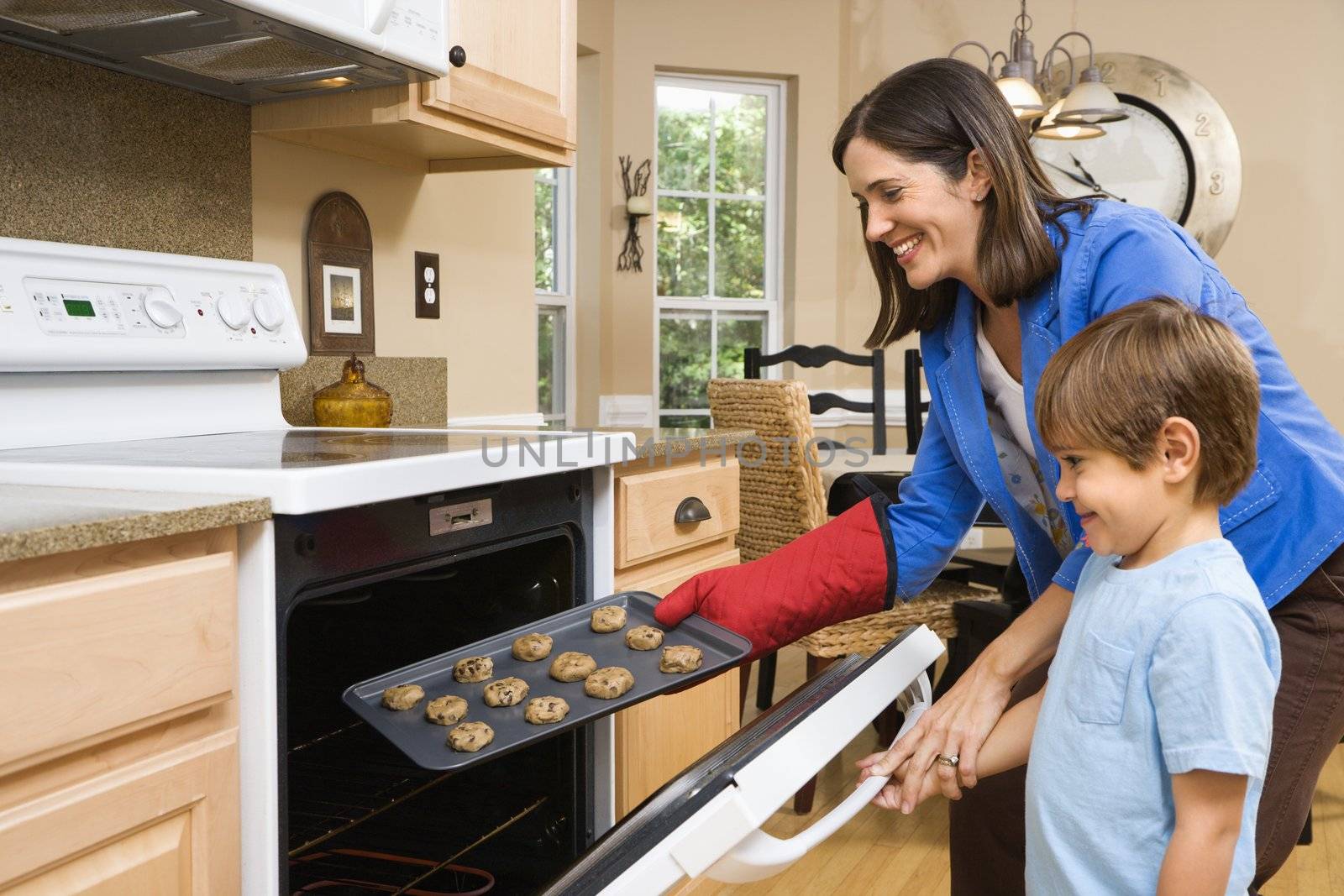 Side view of Hispanic mother and son putting cookies into oven.